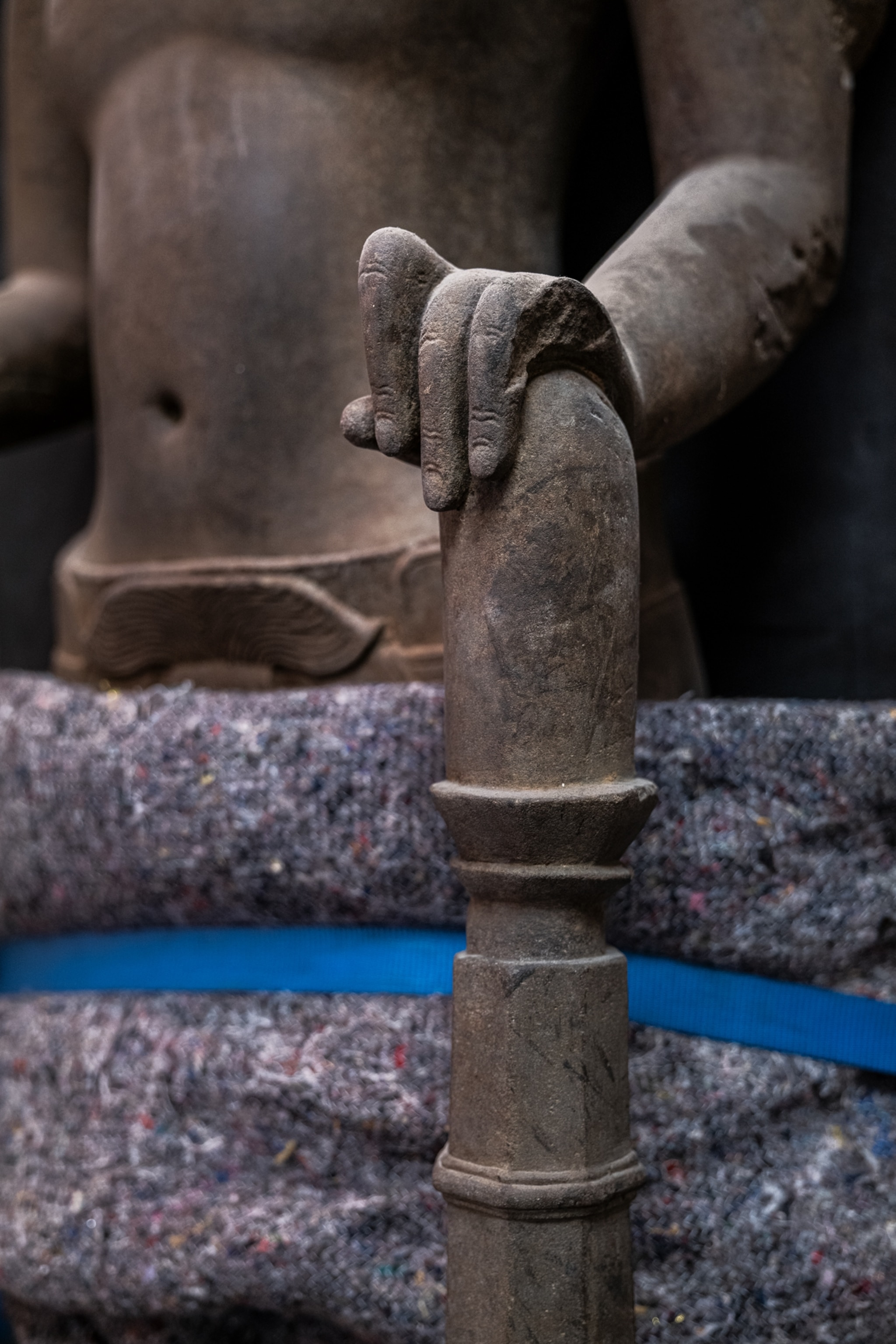 Close up image of a wood statue's hand on a staff with the stomach in the background.