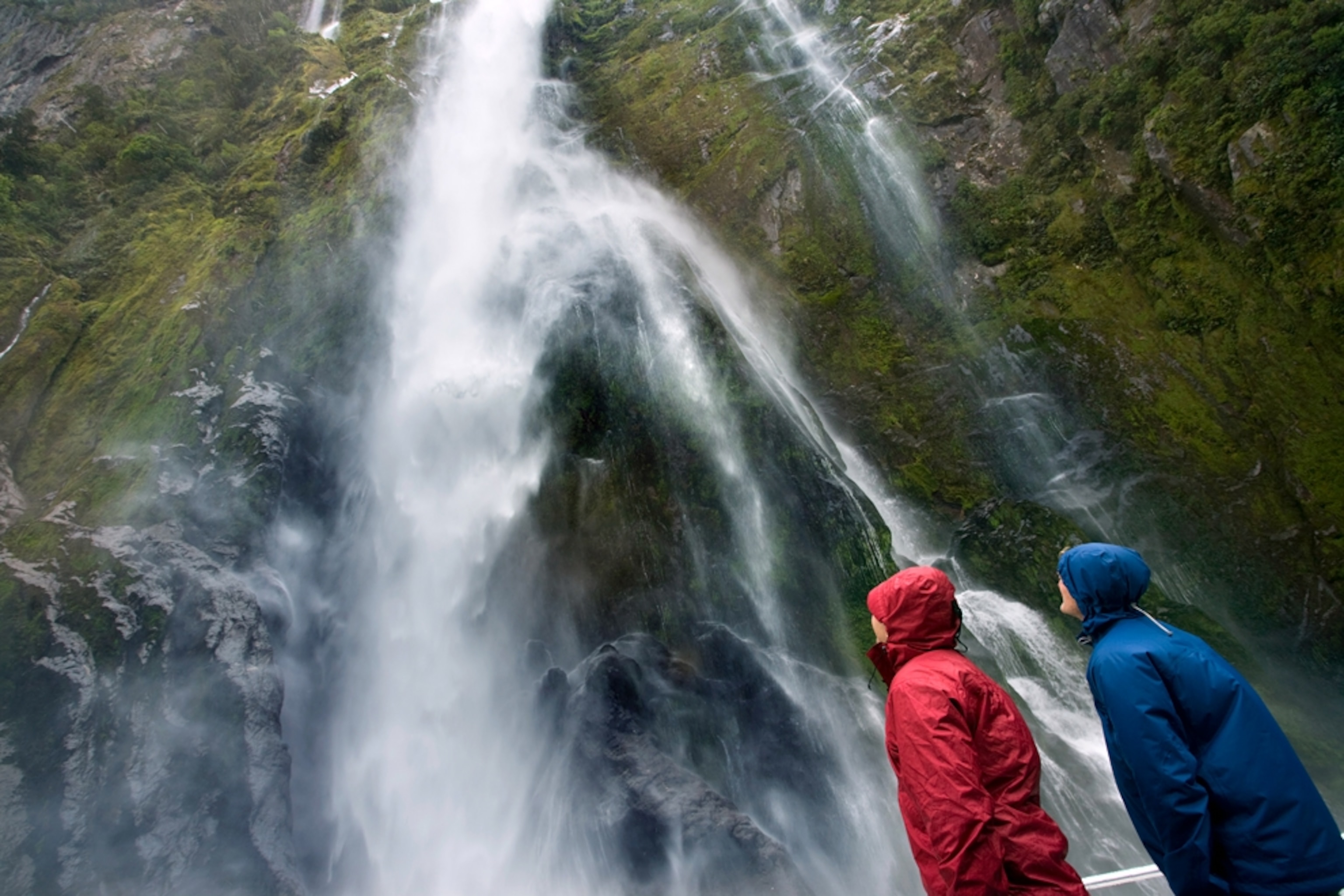 visitors near a waterfall in Milford Sound, Fiordland National Park, New Zealand
