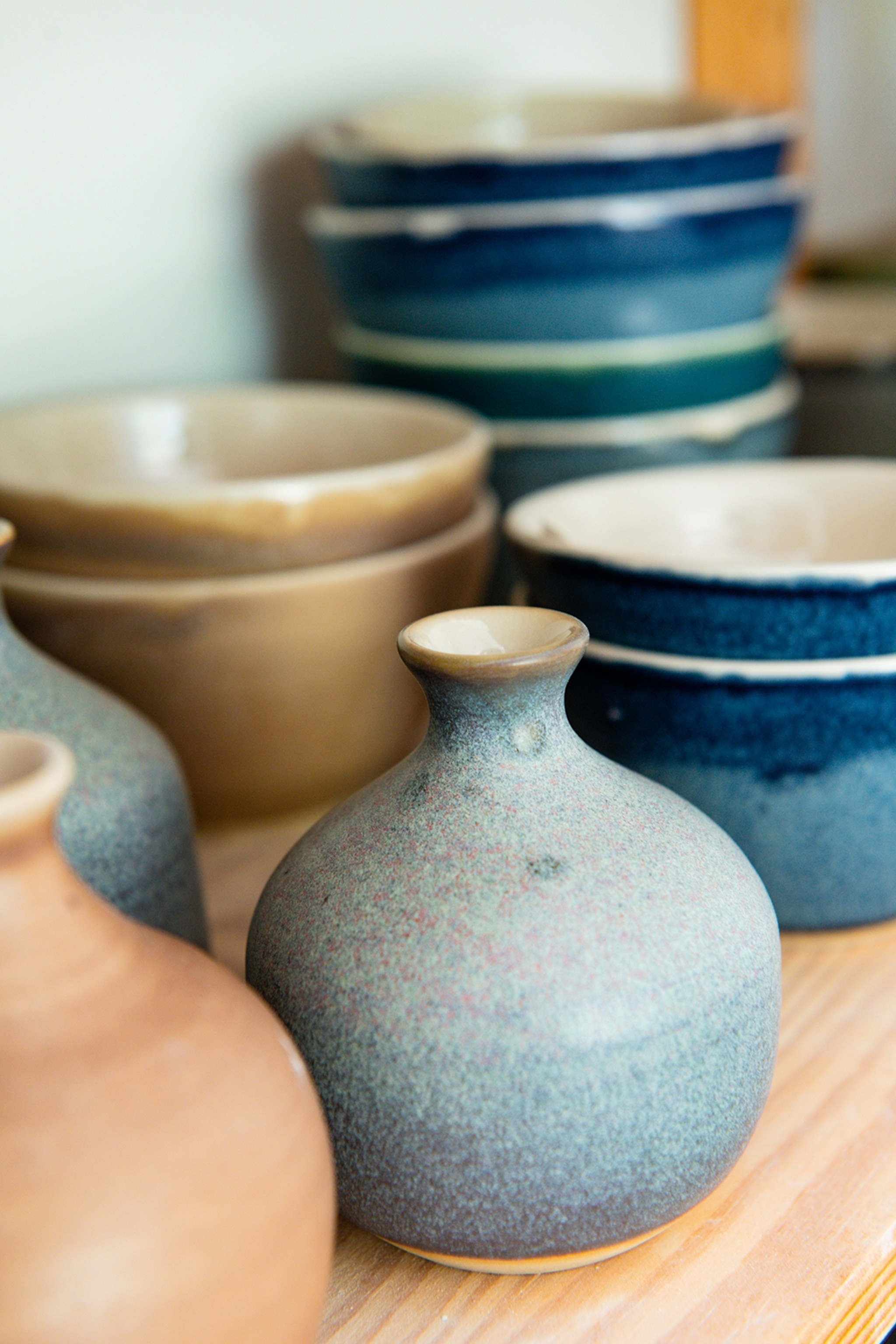 A selection of burnt ceramic bowls and vases on a simple wooden shelf.