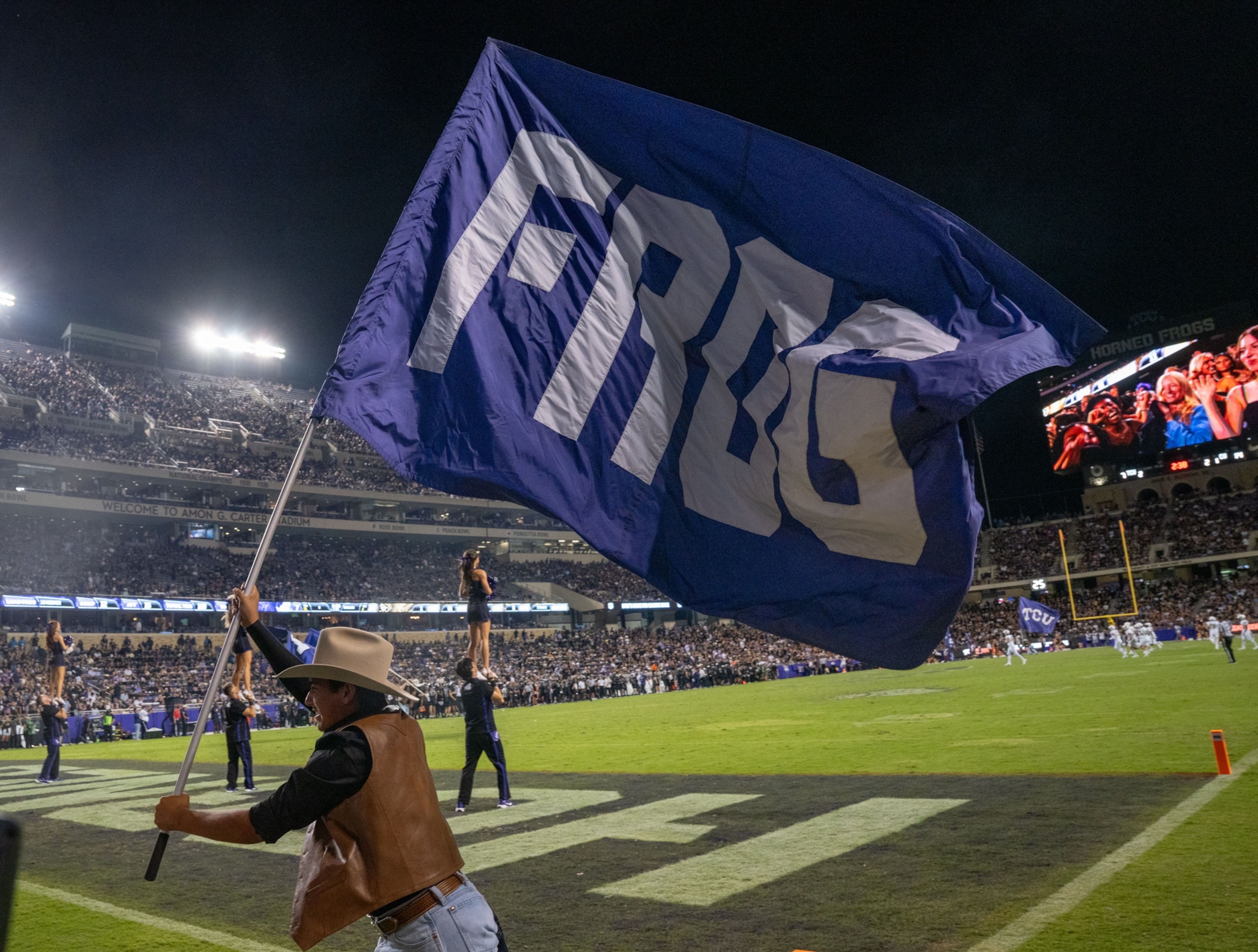 A student group running on football field with blue flag with white word FROG.