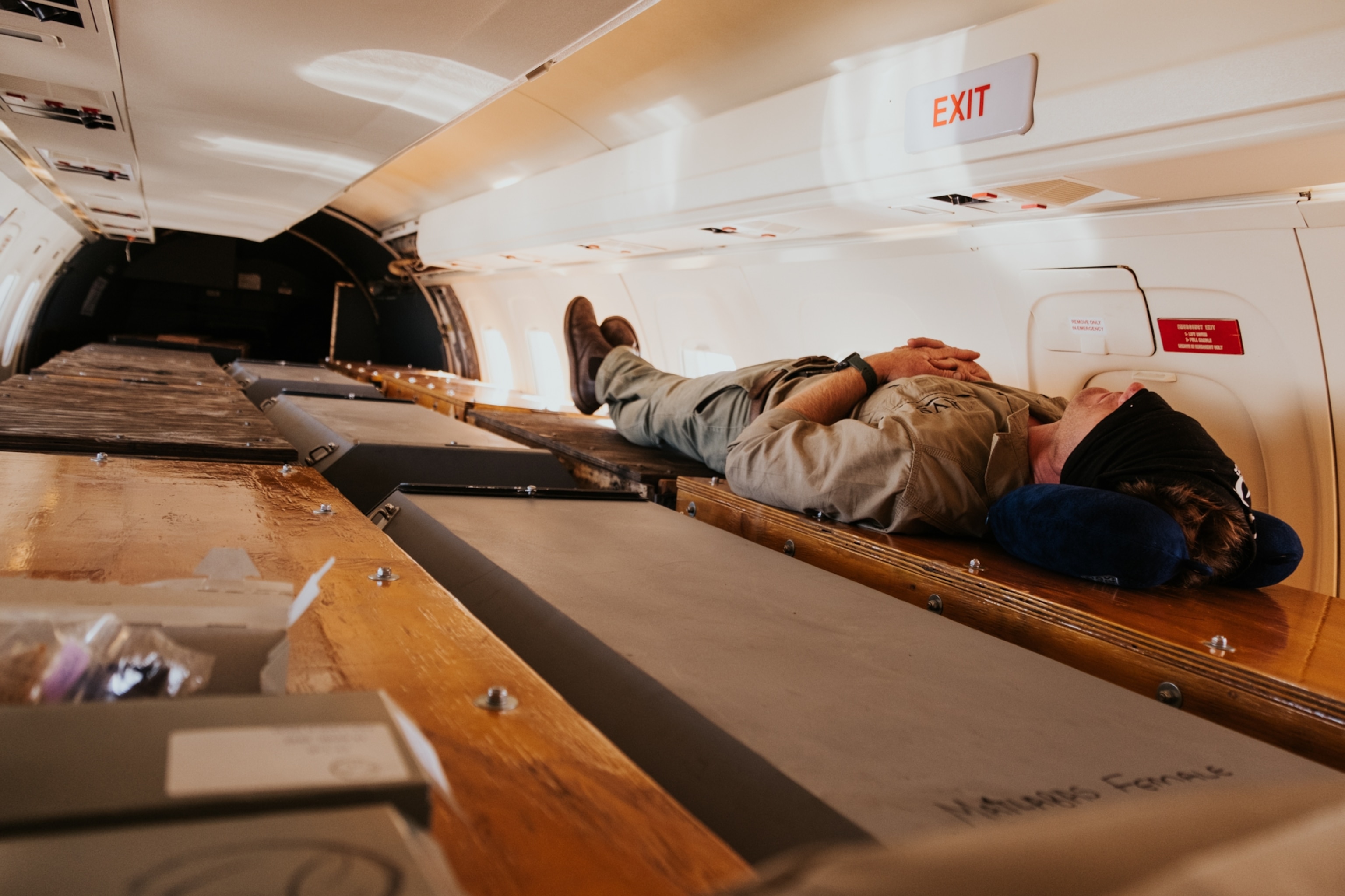 A person resting atop densely packed large crates inside a plane cabin.