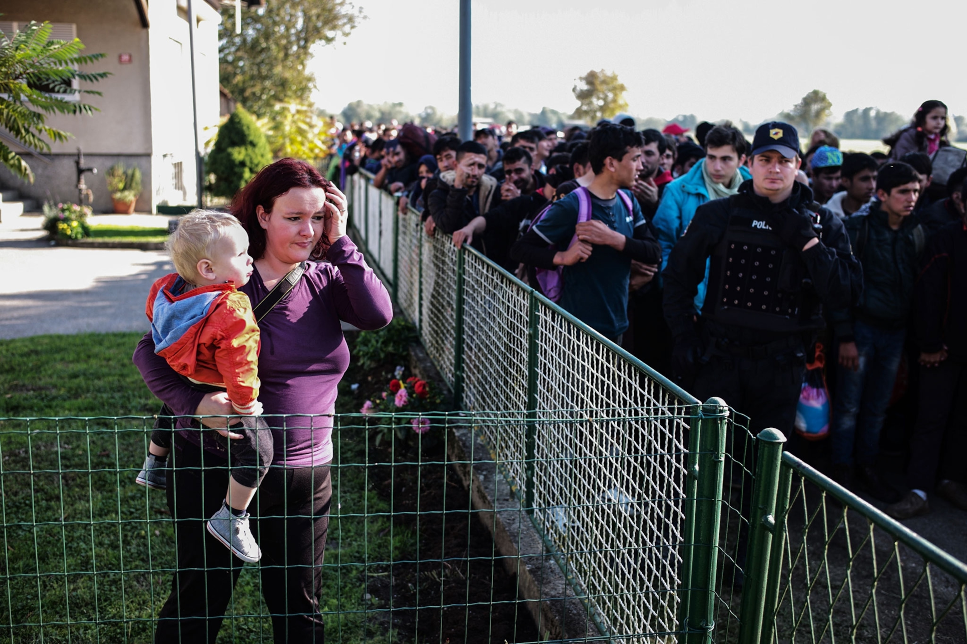a local Slovenian woman looking at refugees walking past her home