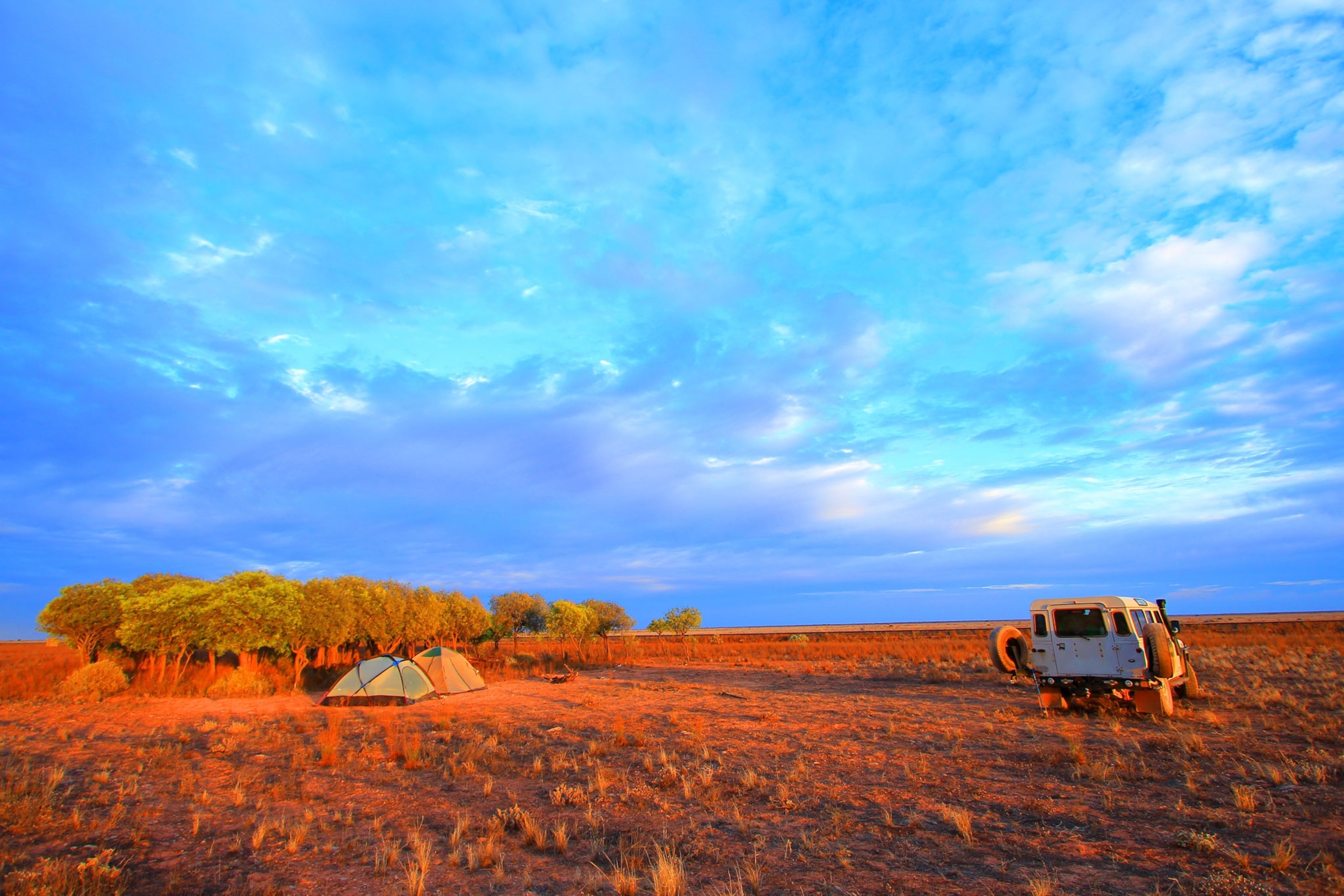 Red-coloured outback landscape with two tents and a jeep parked nearby