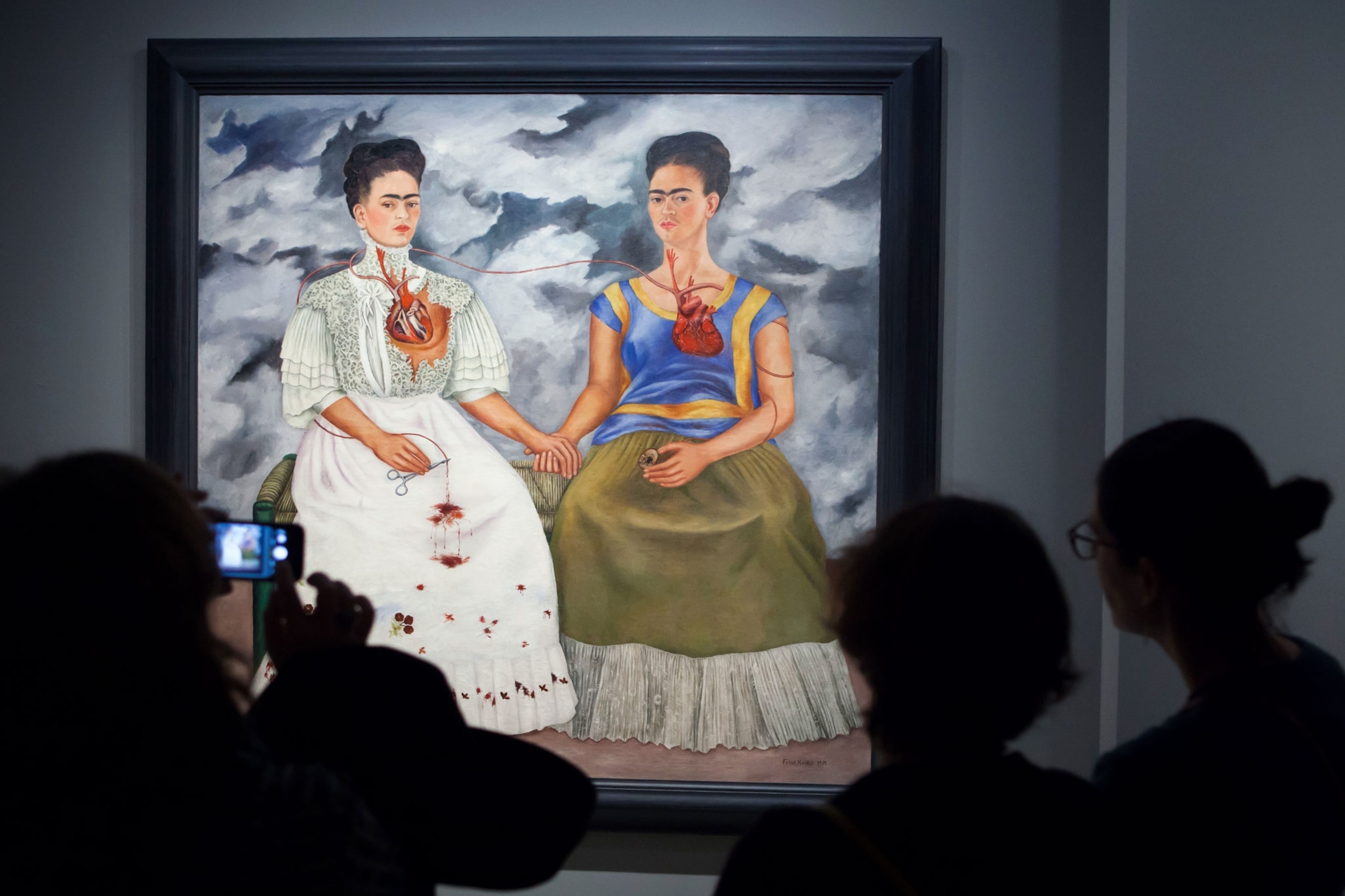 people in a museum looking at a painting by Frida Kahlo