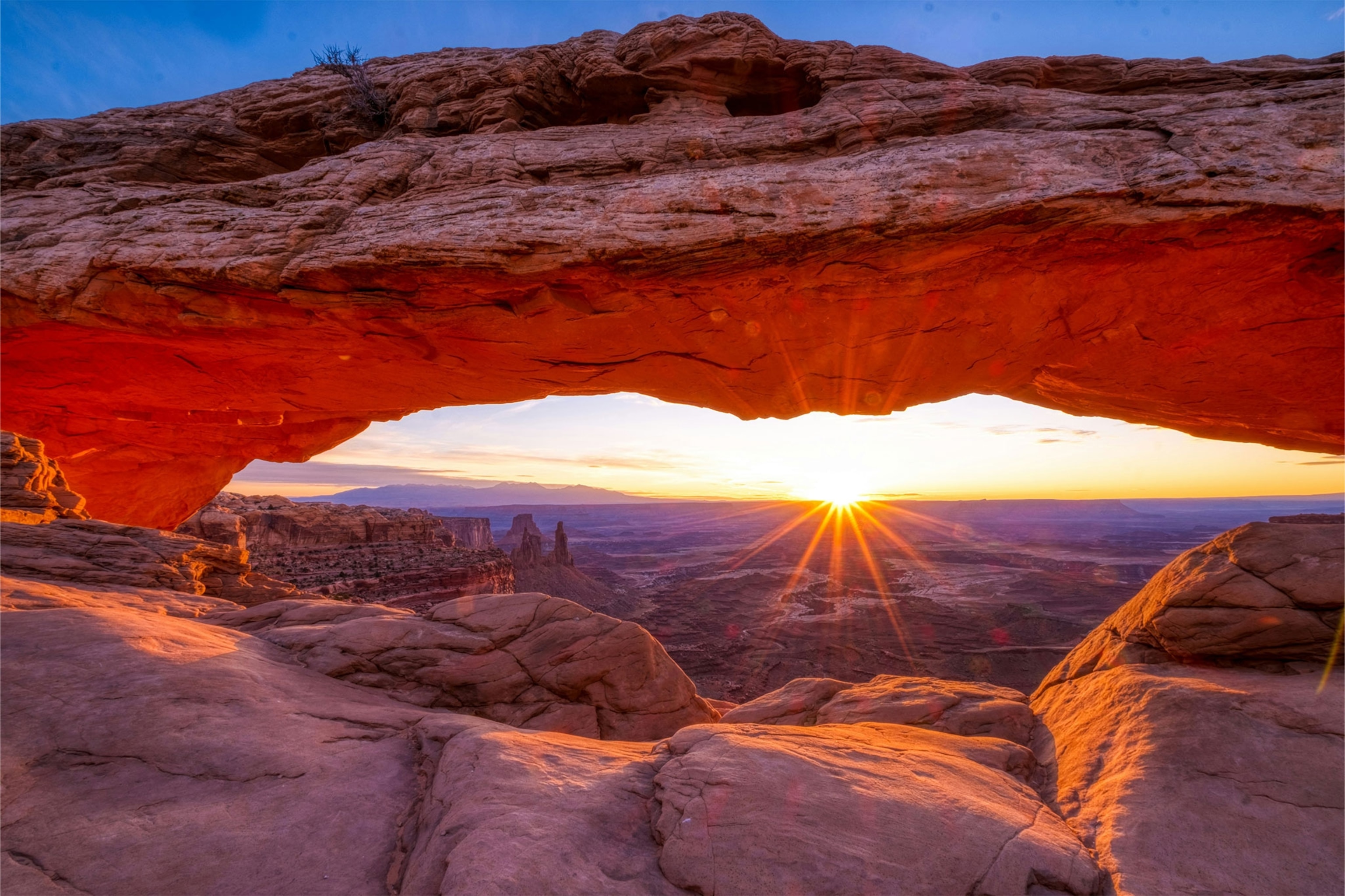 Sunset view through red rock arch with canyons below