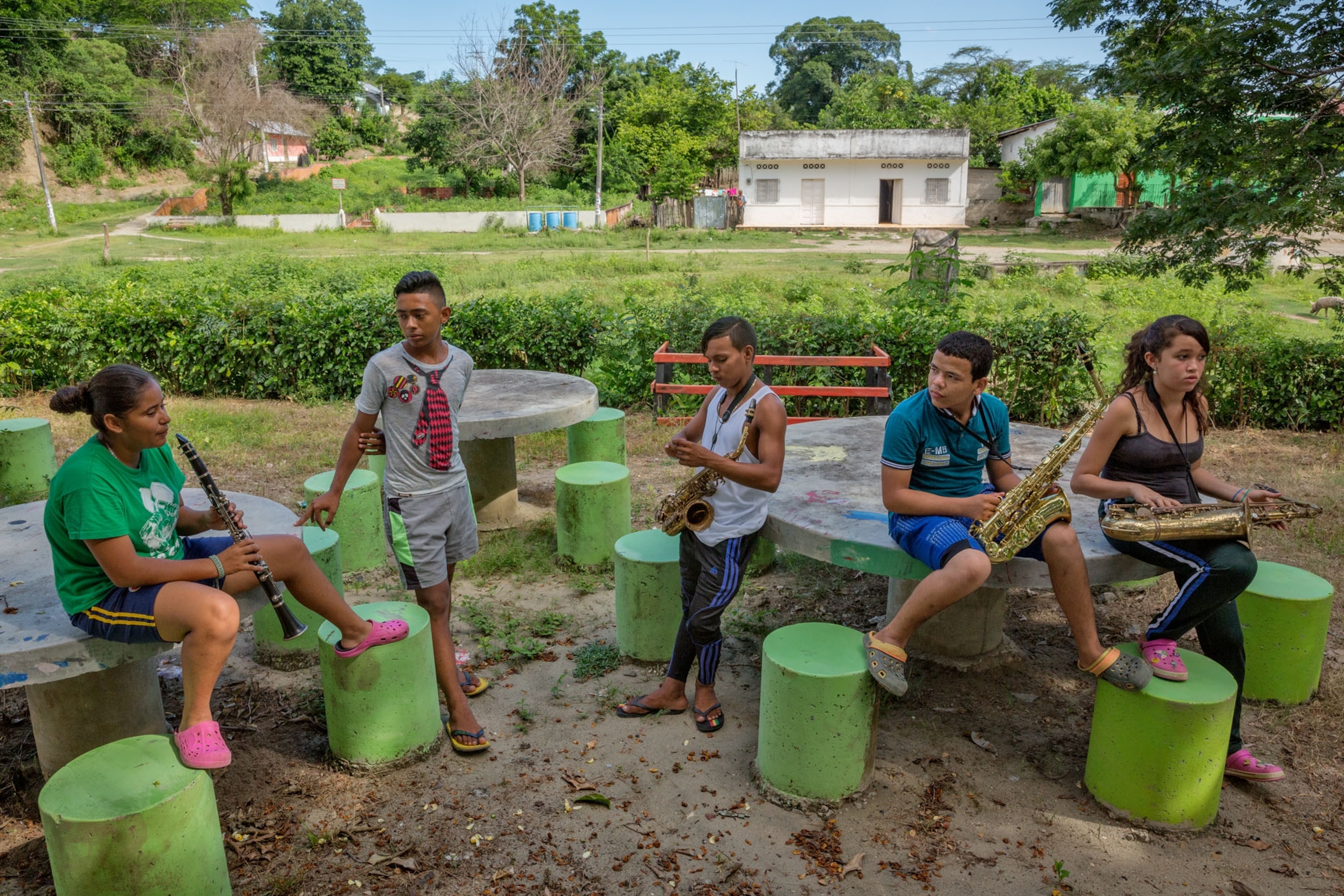 5 children with various instruments in hand sitting outside by cement tables and chairs