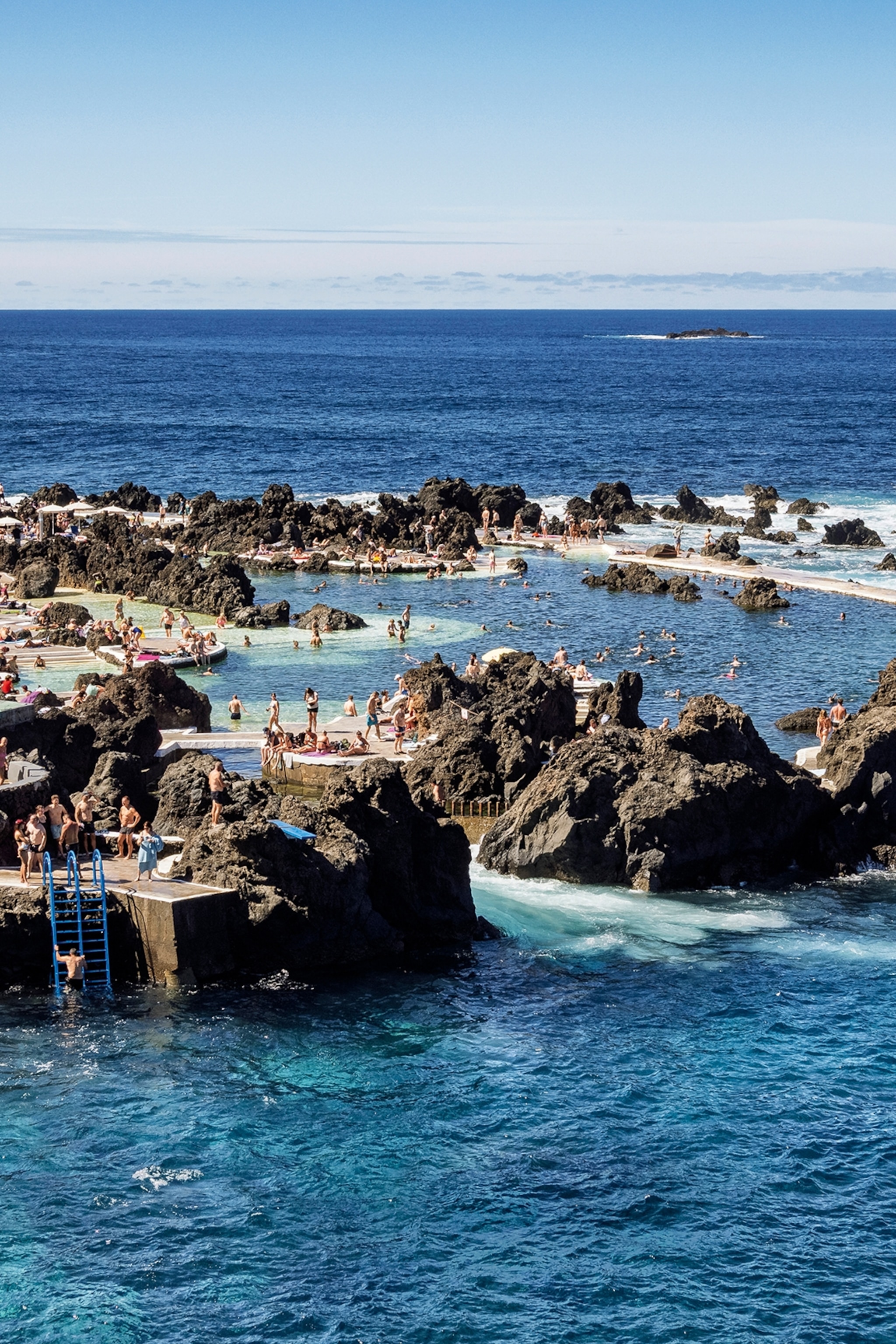 Natural pools leading into the ocean with lots of visitors bathing and tanning on the rocks.