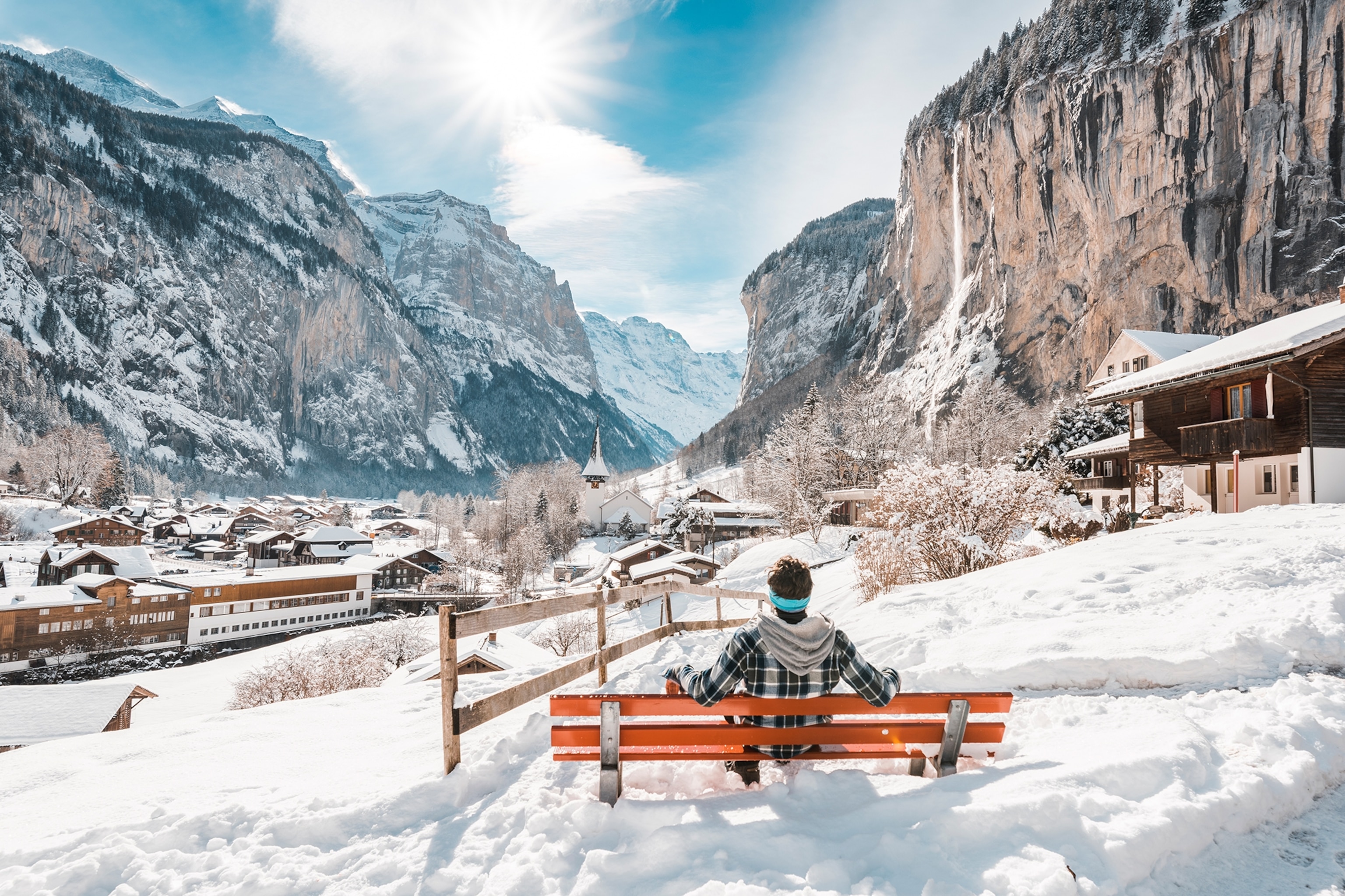 A man in a plaid jacket sits on a bench overlooking the Lauterbrunnen Valley during the winter in Switzerland.