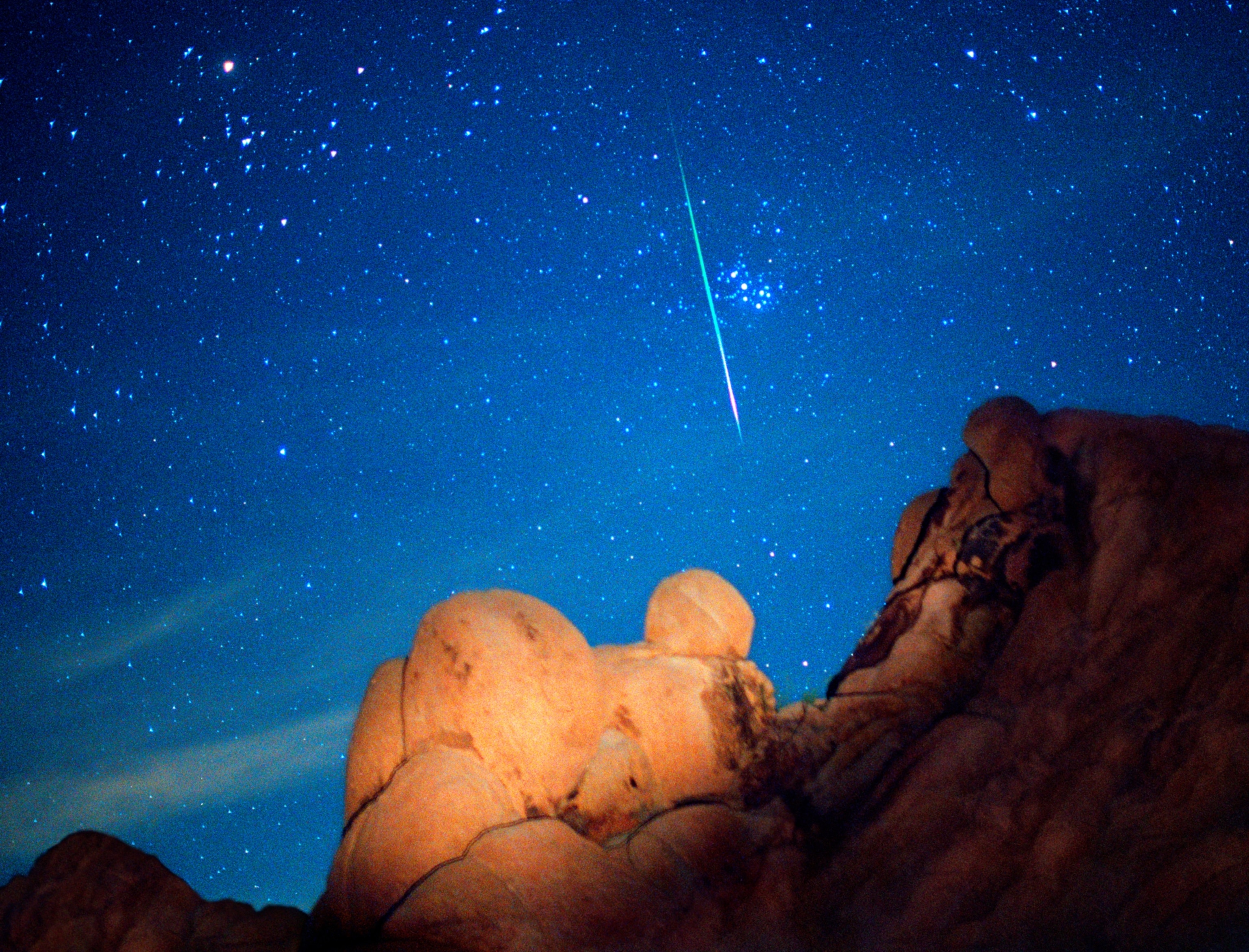 The white streak of a meteor slicing through a starry sky above rocky formations