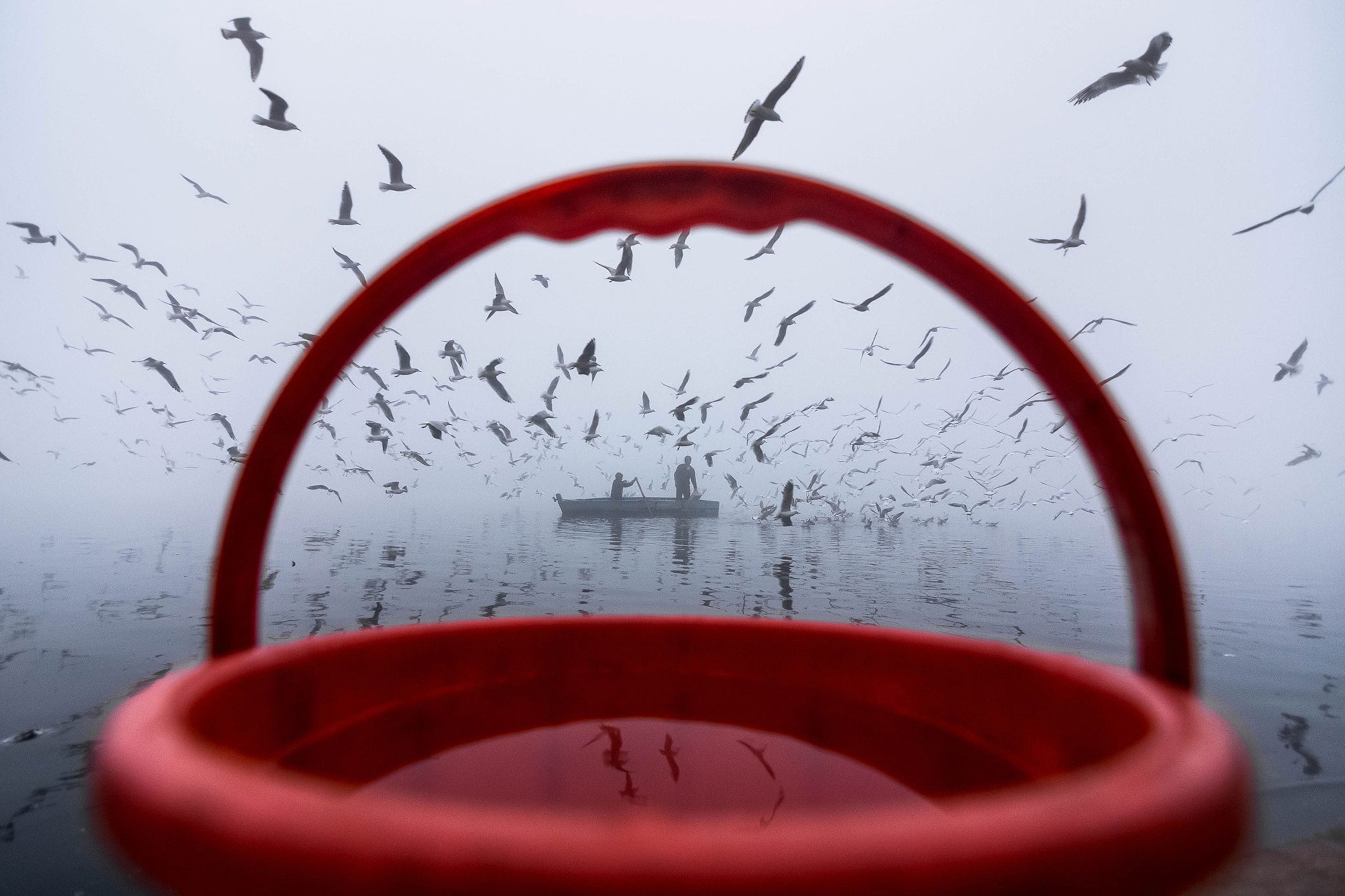 a red bucket framing fishers and birds on the banks of a river