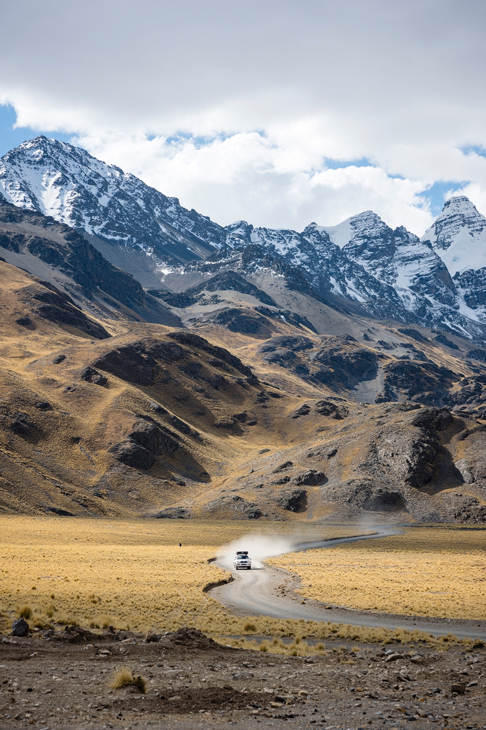 A car driving down a dirt road towards a dense mountain range.