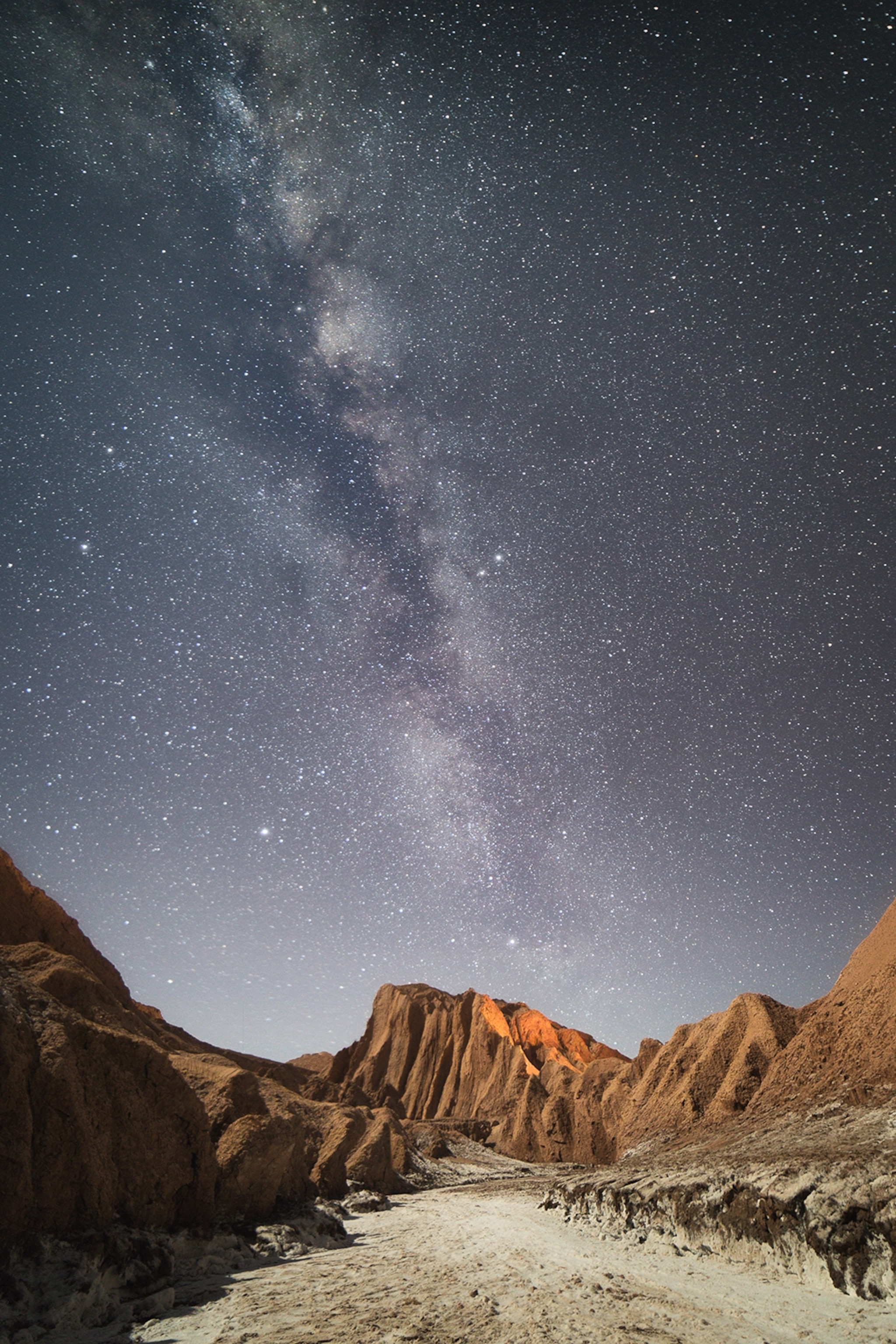 A desert landscape enclosed by hills at night, as stars dot the sky.