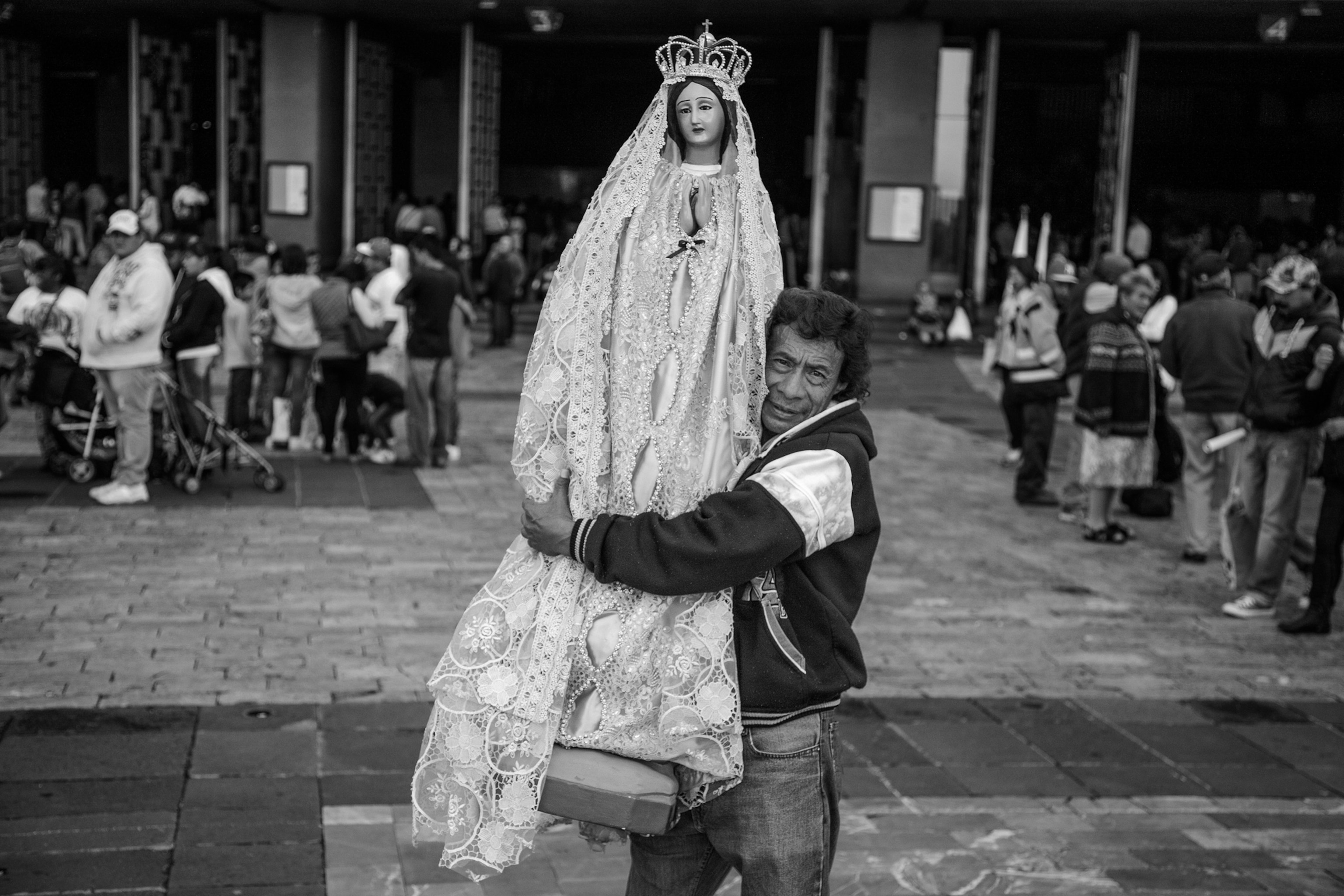 A man holds a large doll-like figure of a woman wearing a dress and crown