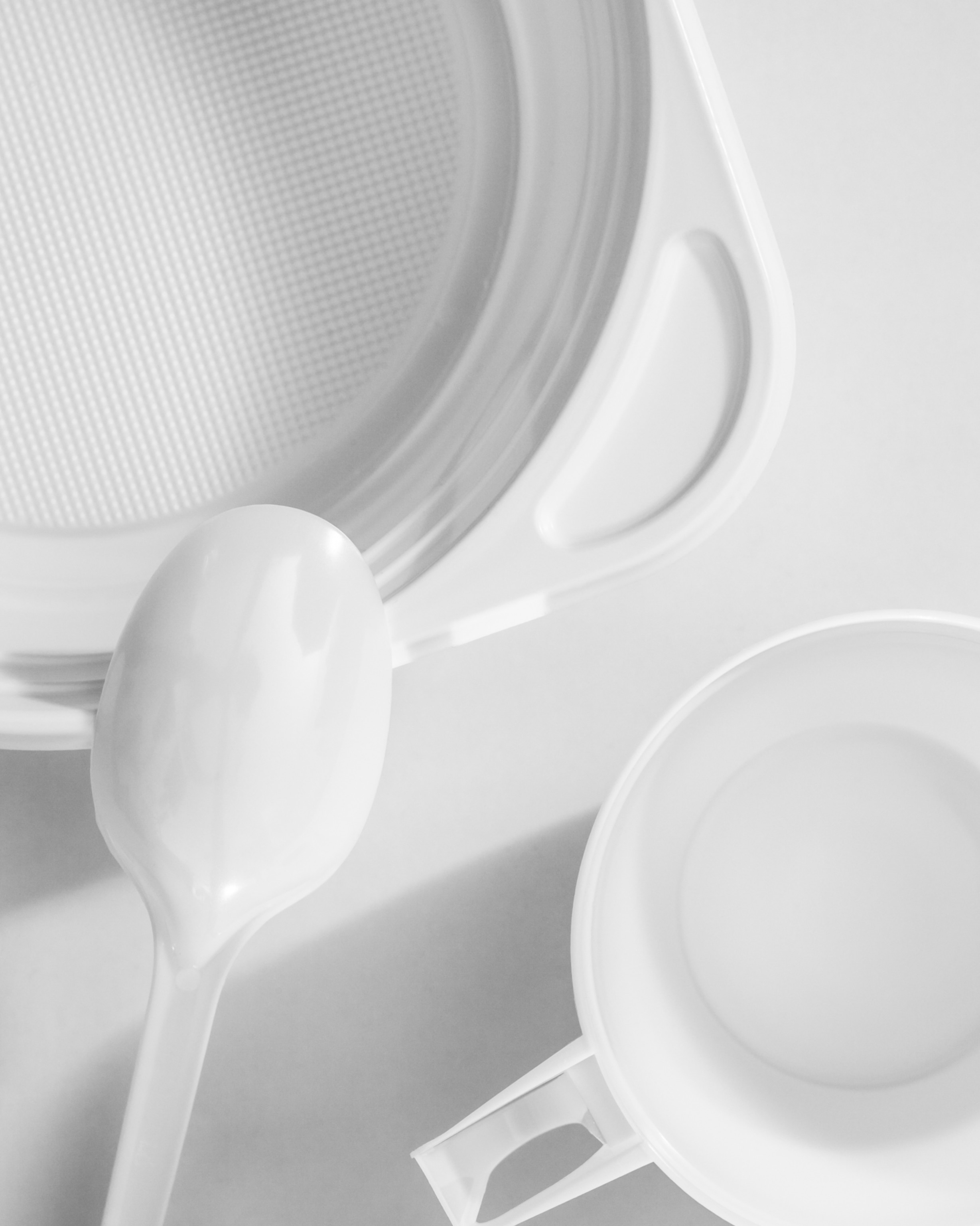A minimalist image featuring a white plastic spoon resting on a white plastic textured bowl, next to a white plastic measuring cup.