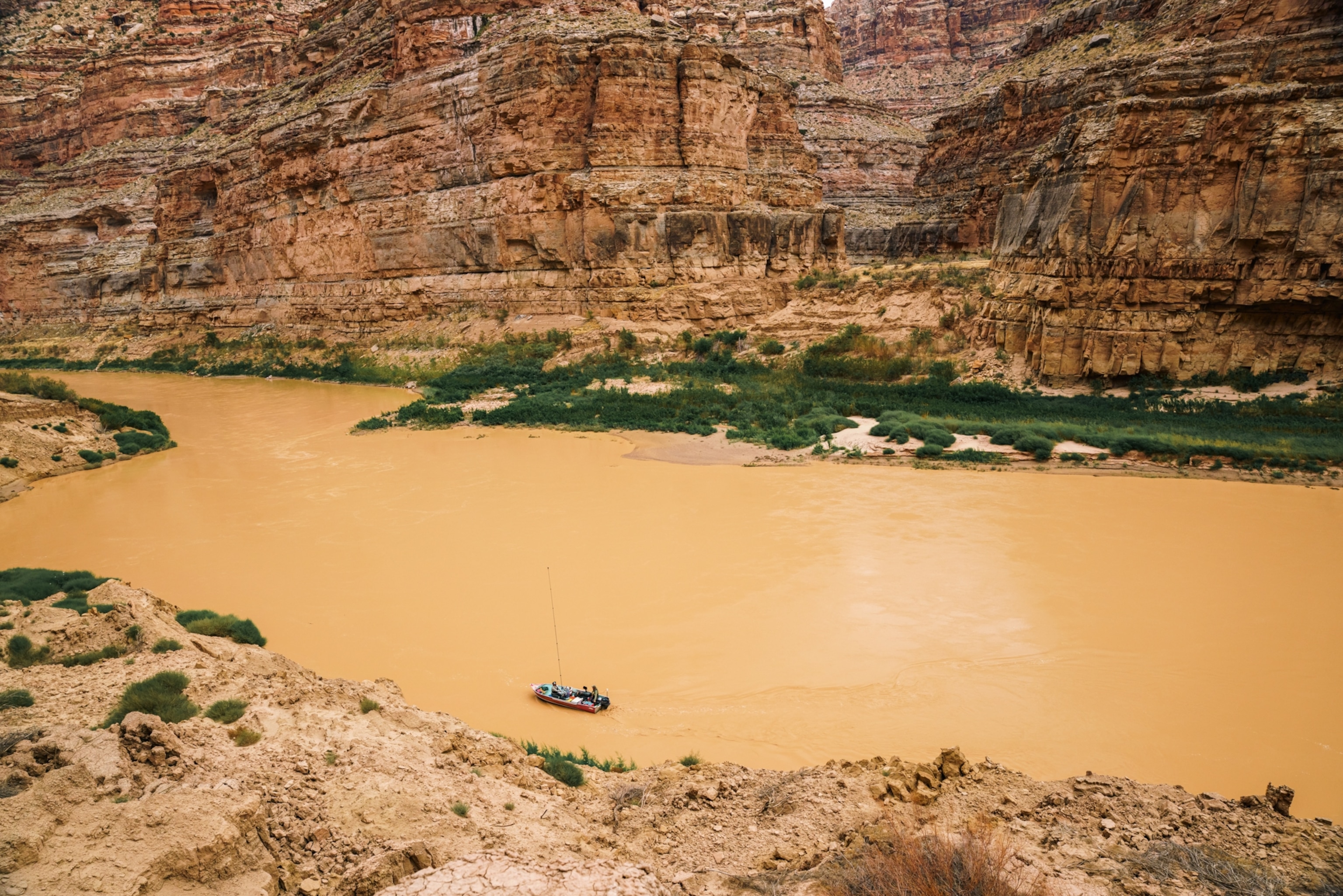 A small boat floats near a dirt shore on an opaque, yellow-brown river.