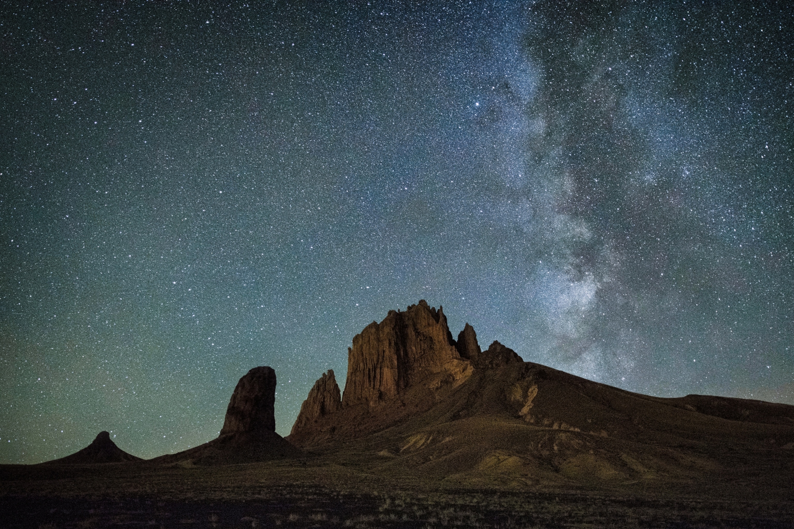 Starry night sky with Milky Way over silhouetted desert rock formations.