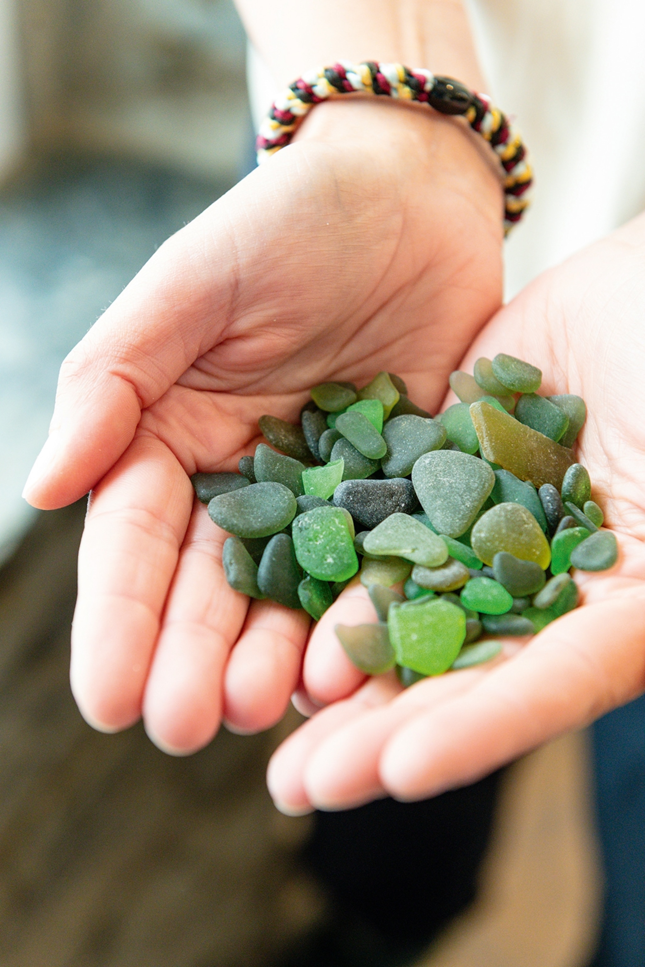 A close-up of the two hands cupping a bunch of sea glass pebbles.