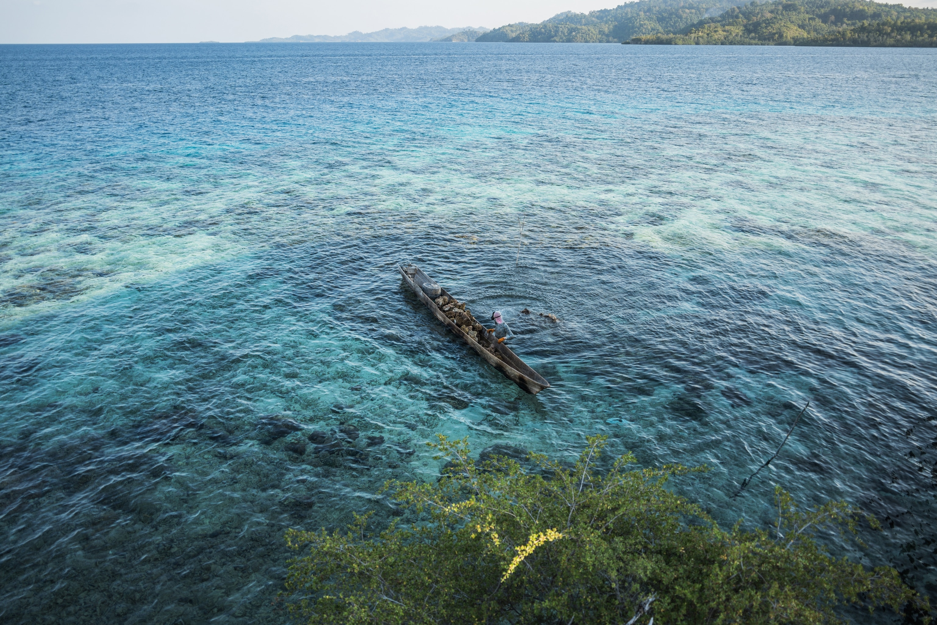 A man in a boat is photographed from above in clear blue waters.