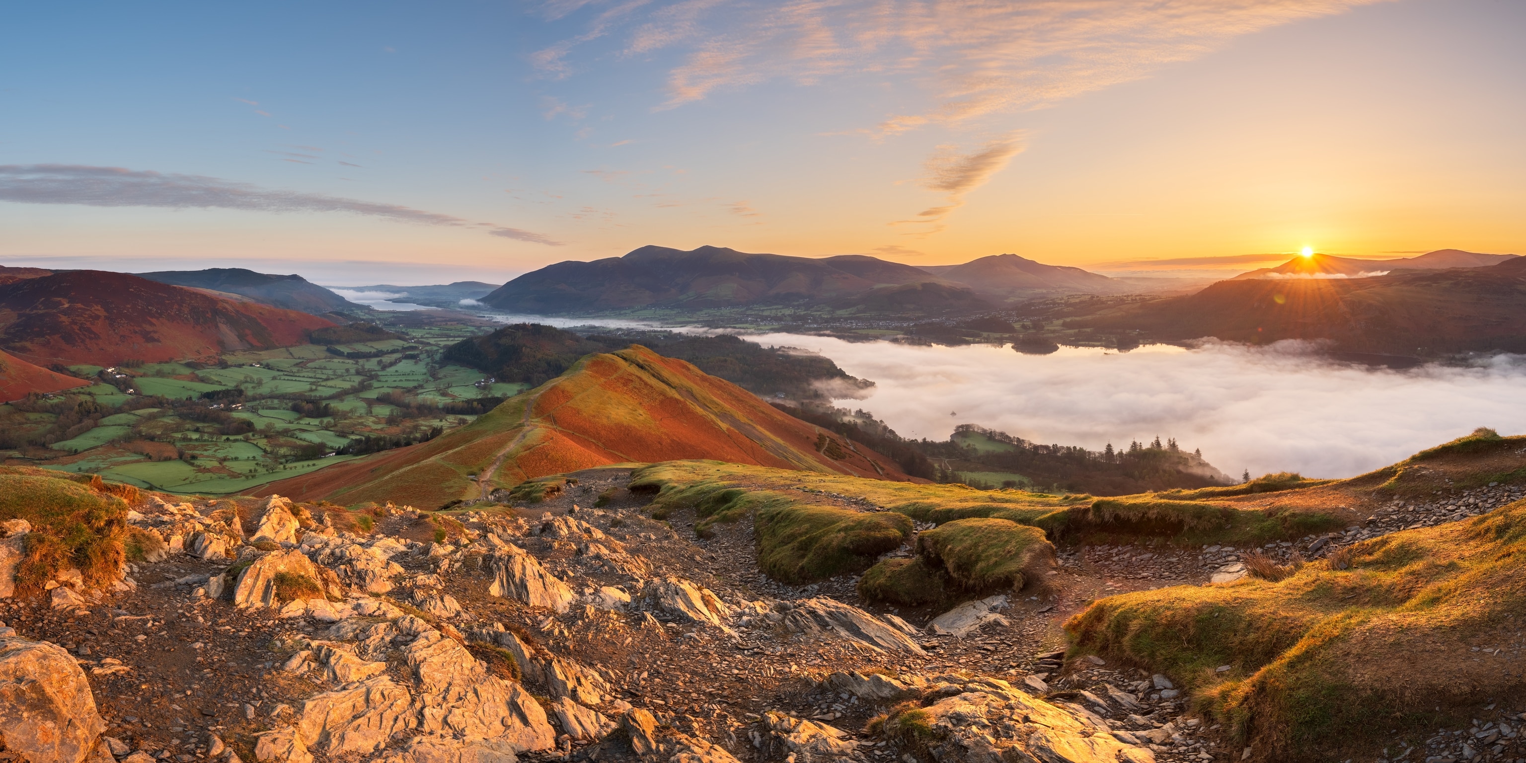 A wide landscape shot of rocky hills and a lake in the a valley as the sun sets on the horizon.