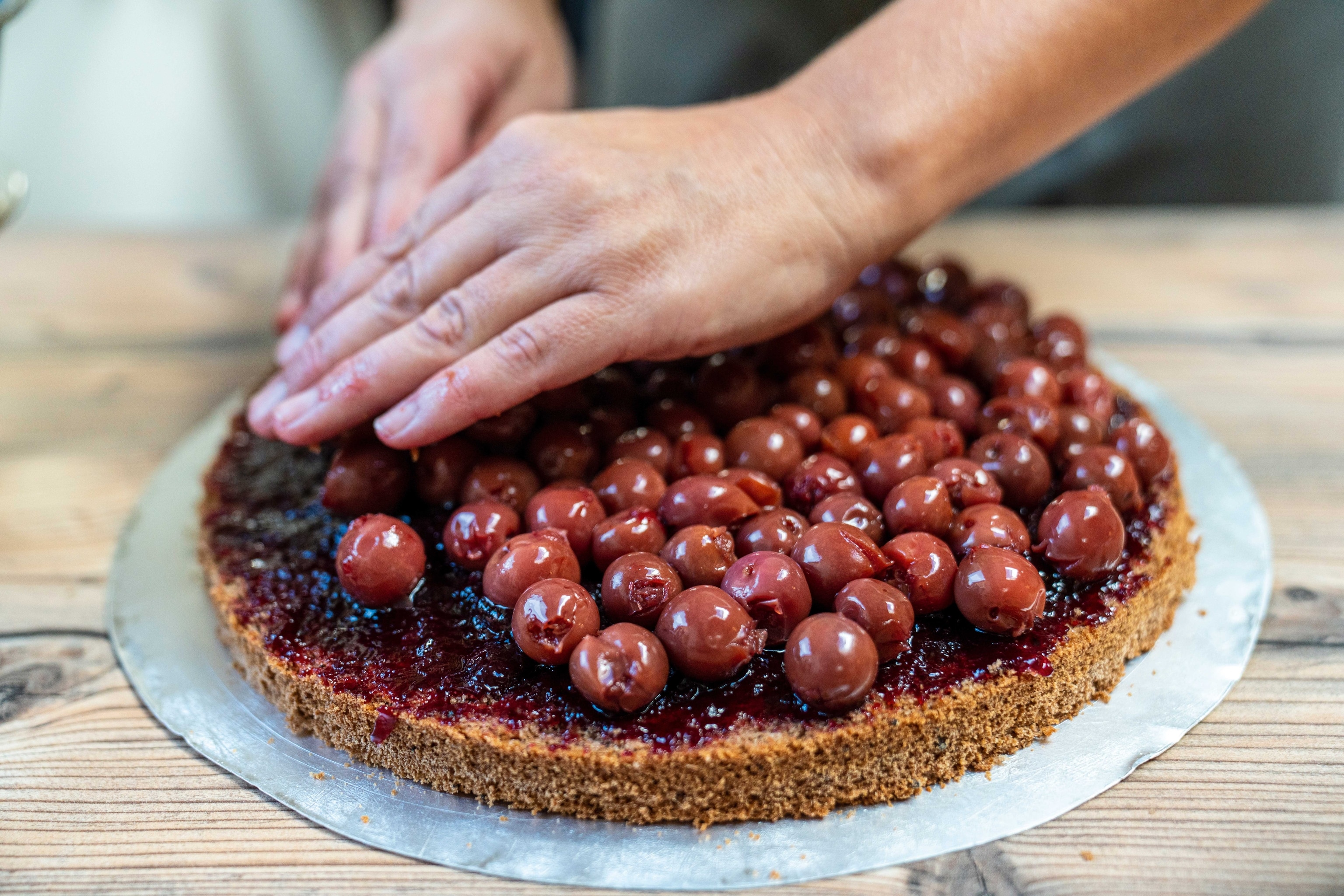 A chef's hands carefully place cherries onto a cake base.