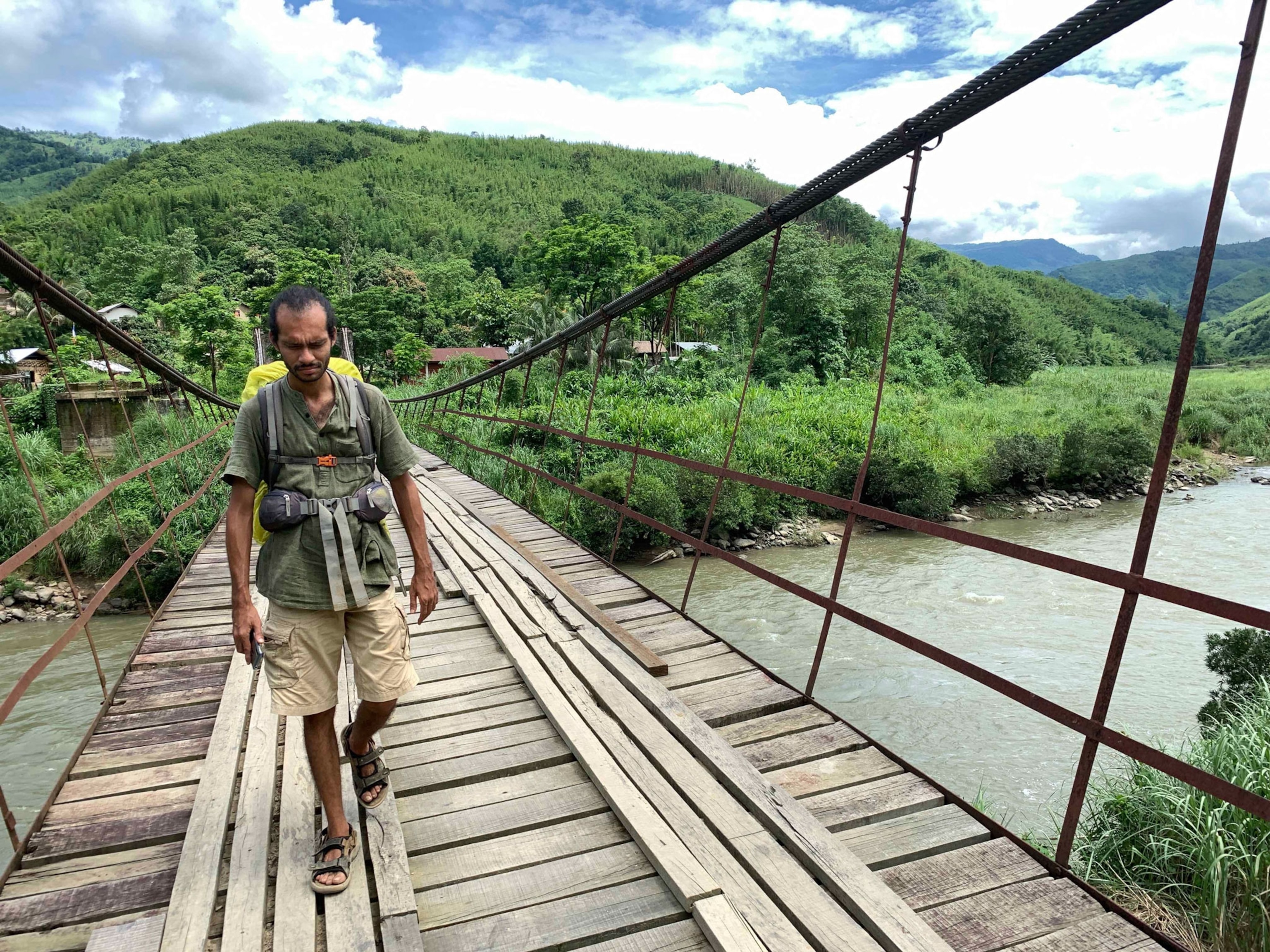 a man walking across a river on a rope and wooden bridge