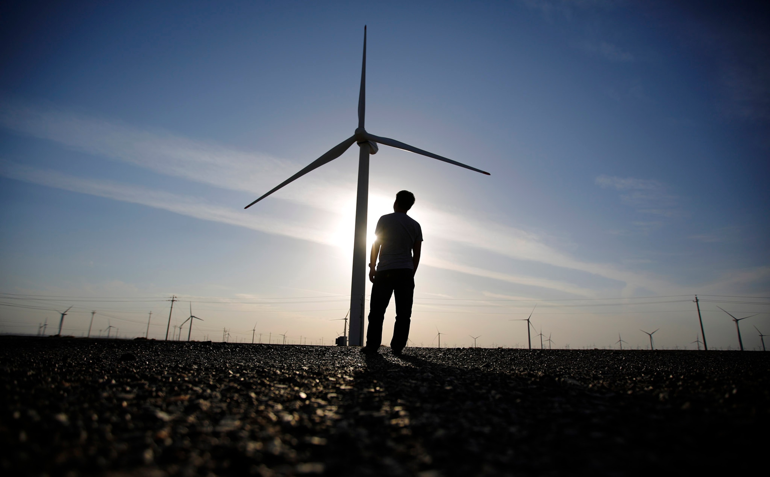 worker stands as he looks at a wind turbine used to generate electricity