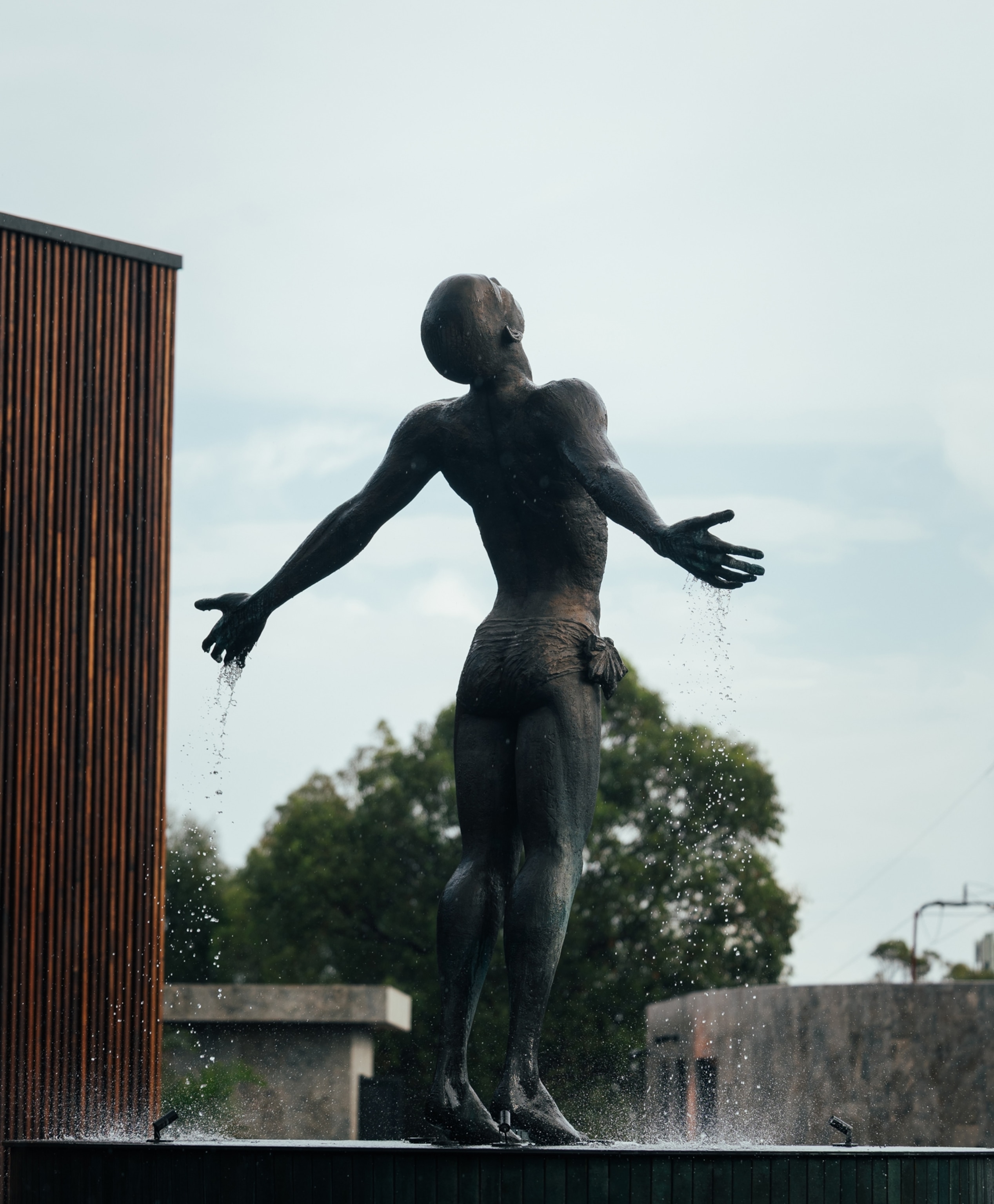 A large bronze fountain sculpture of a human figure stands with outstretched arms as water flows into a pool below.