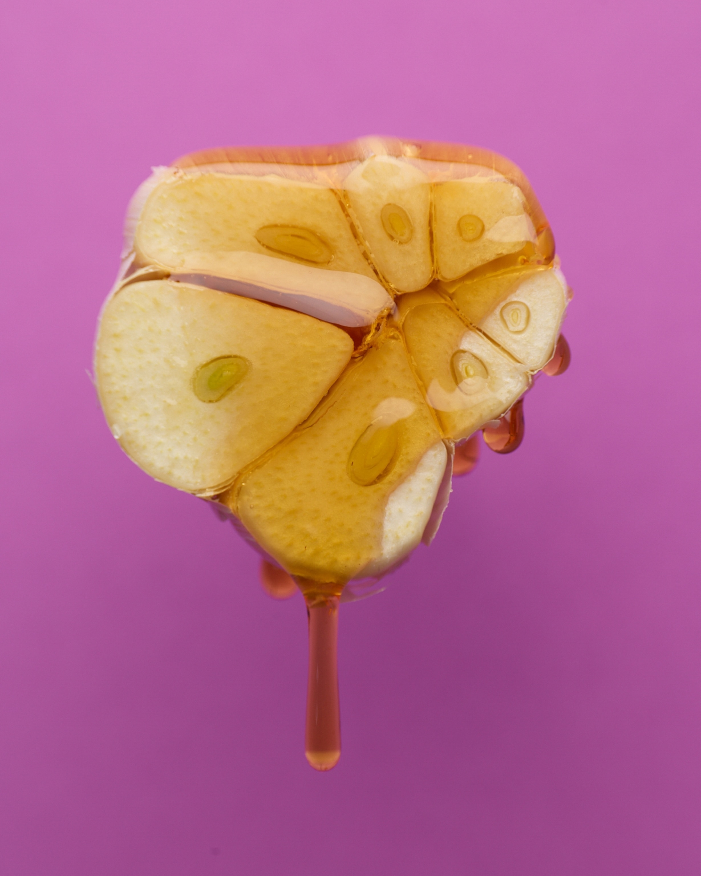 Close-up of a golden honey dripping down a halved bulb of garlic, against a vivid purple background.