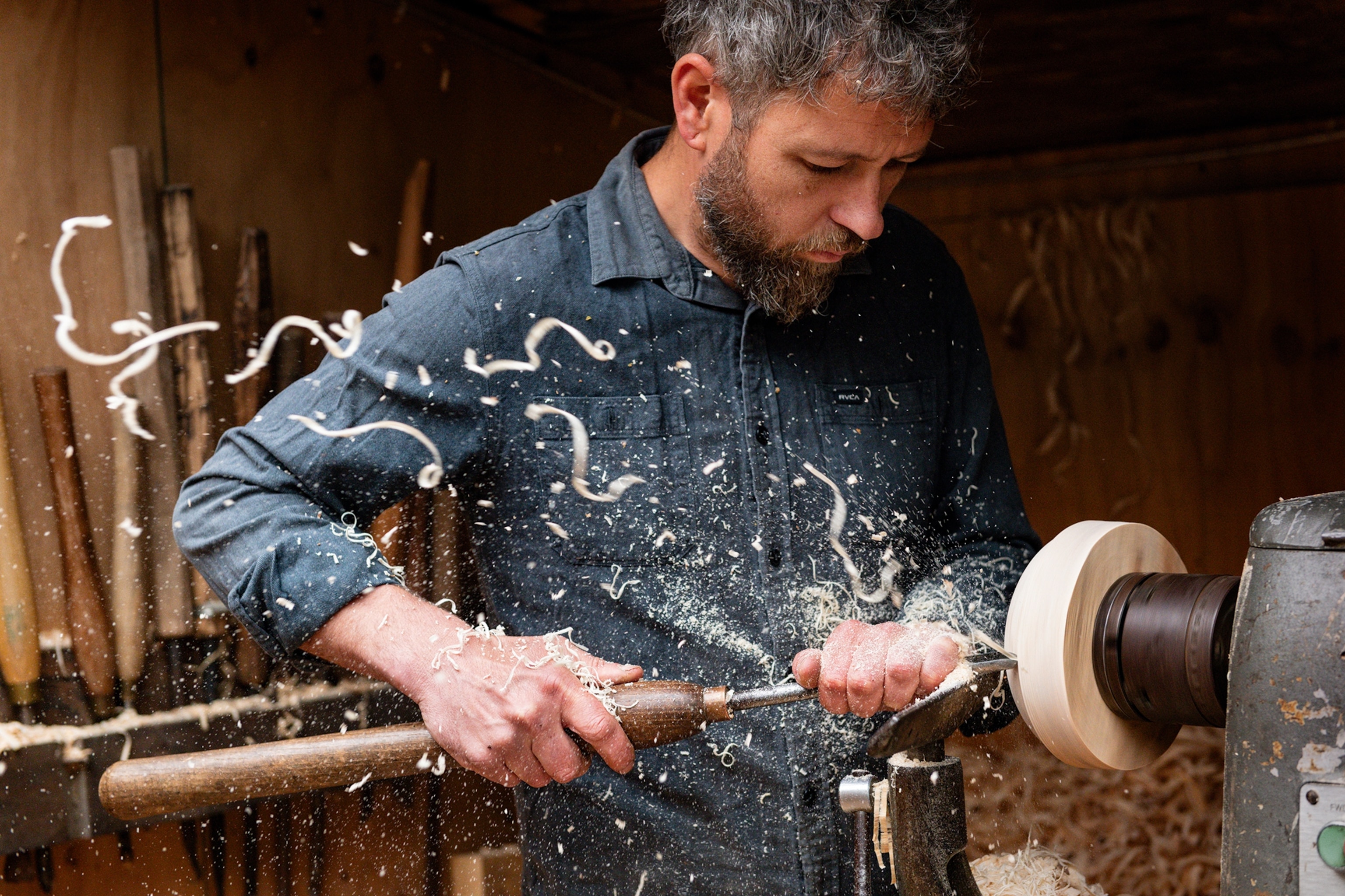 A dynamic shot of a man carving a wooden bowl on a spinning machine.