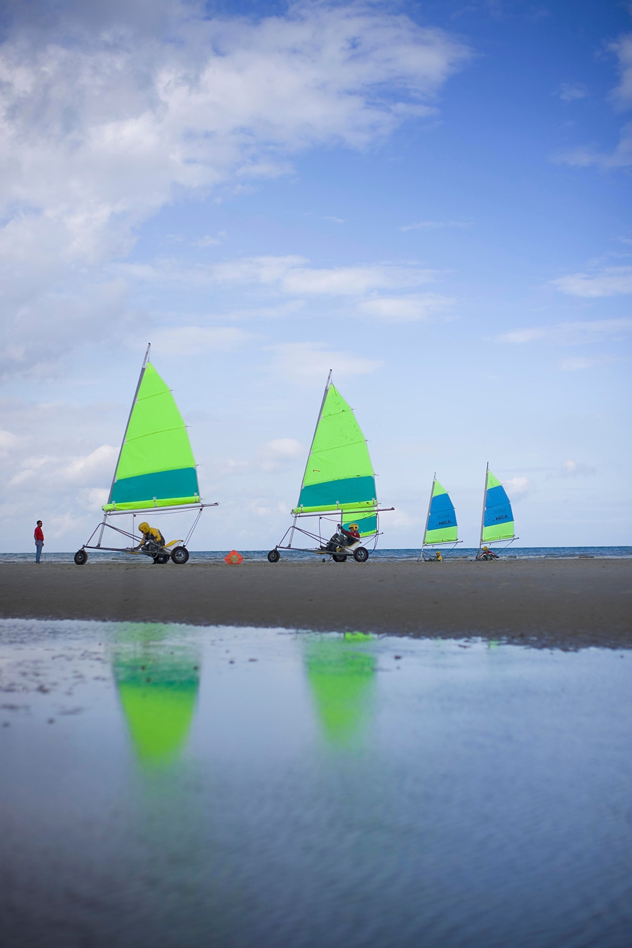 Sand sailors on sandy beach with water in foreground.