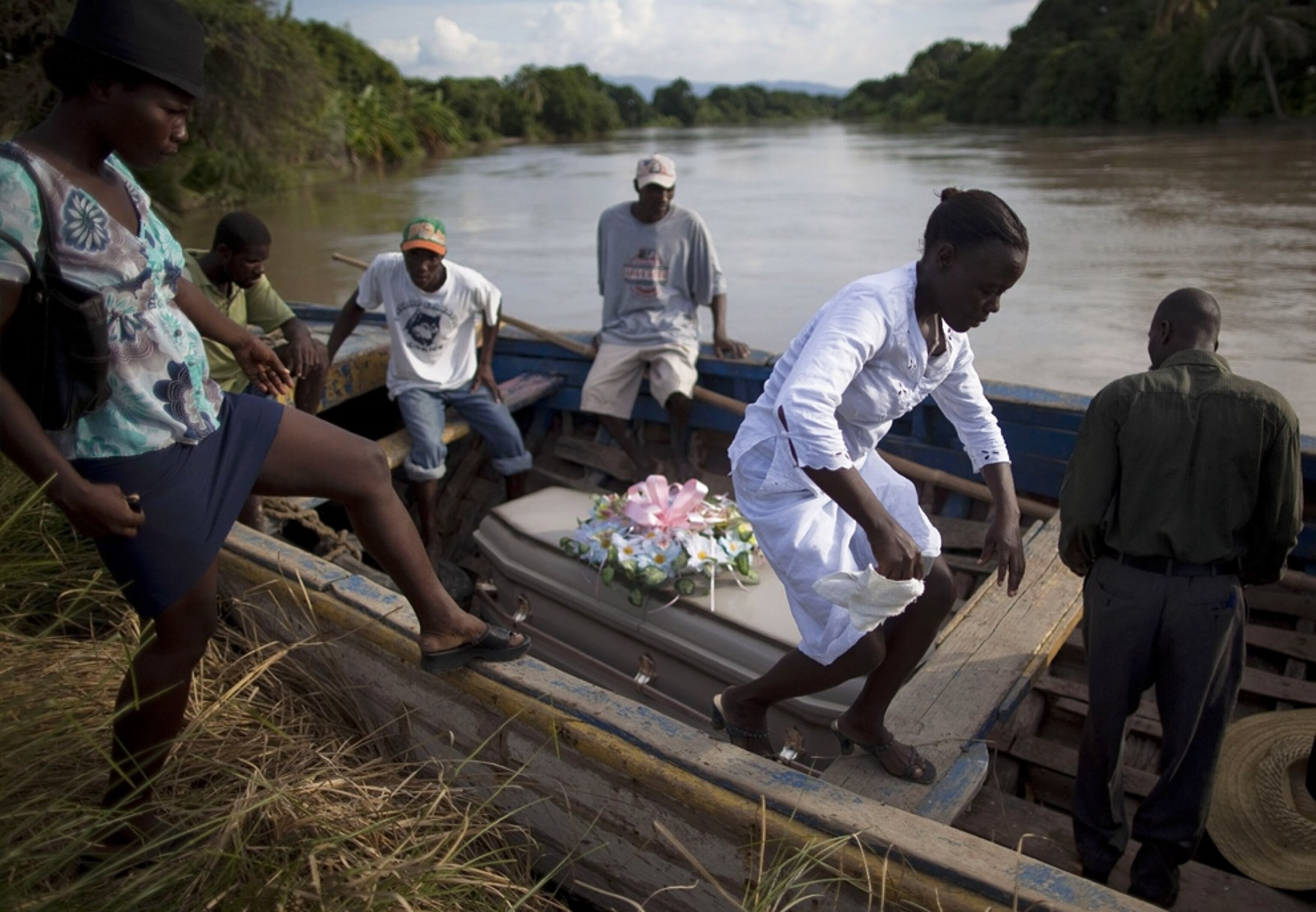 People climb into a boat, where a coffin rests, for a journey on a Haitian river -- picture from a photo gallery on the one-year Haiti-earthquake anniversary