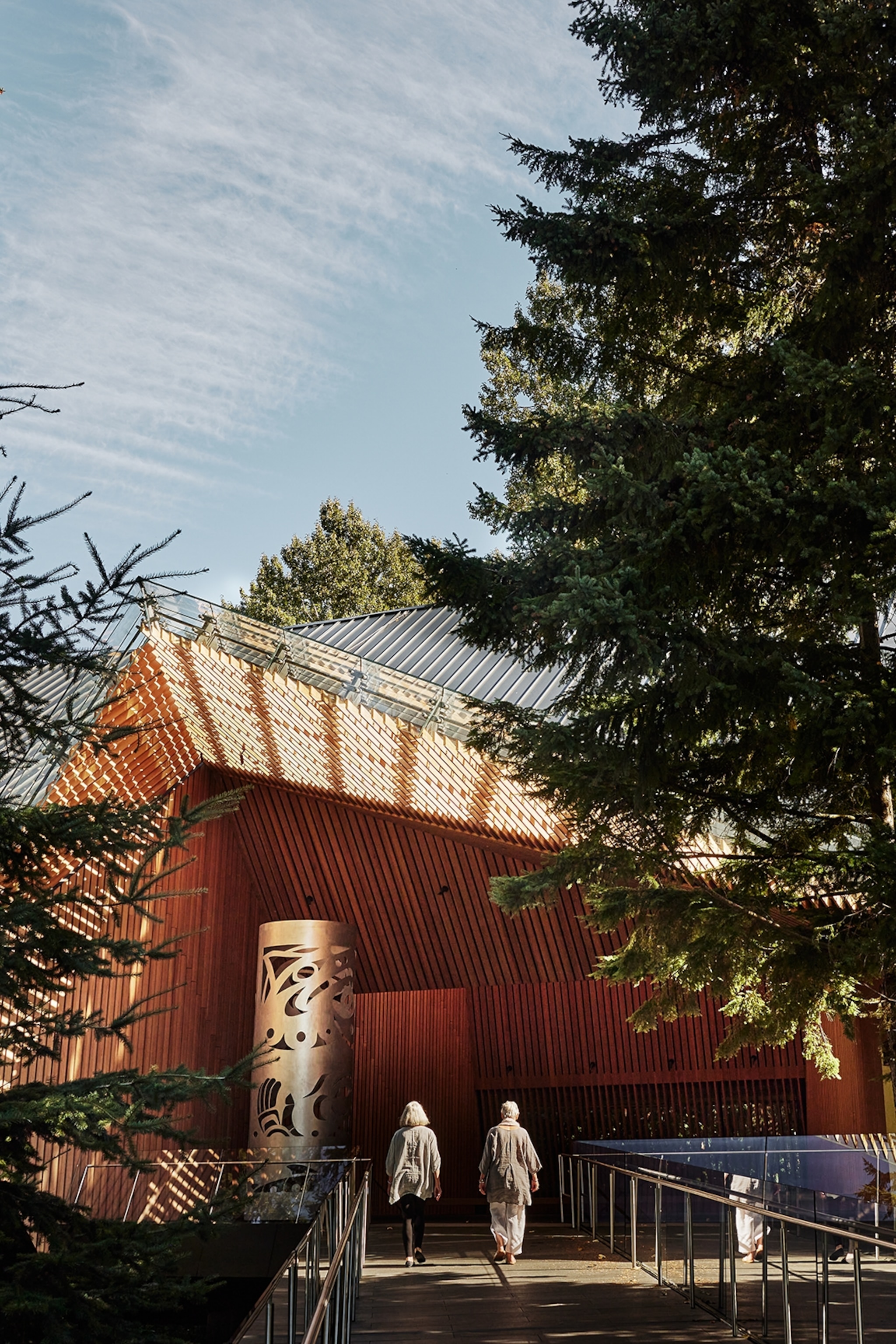 A modernist, wooden cabin museum in the middle of a pine forest with a boardwalk to the entrance.