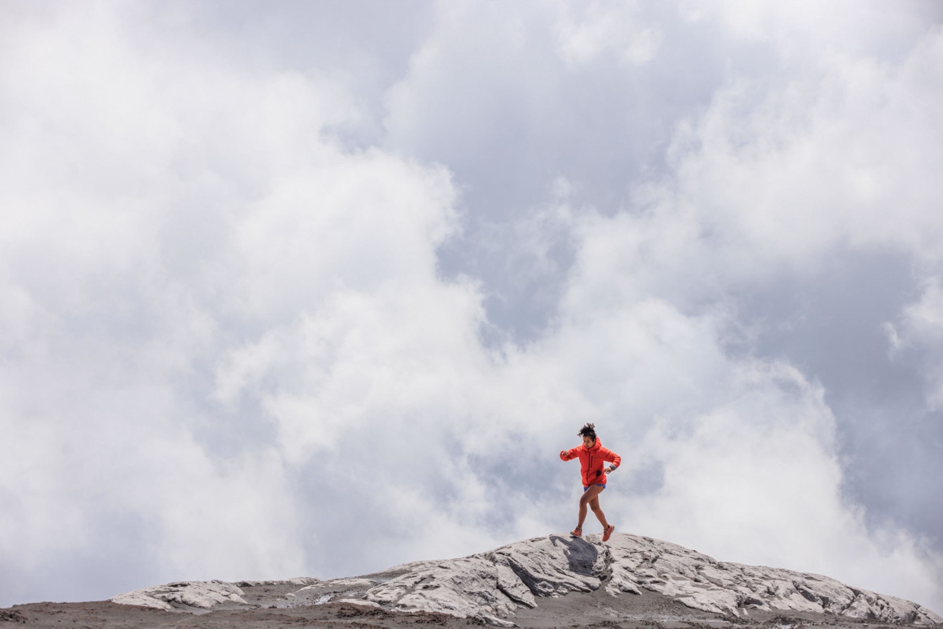 a woman runs along a rocky rim with clouds in the background