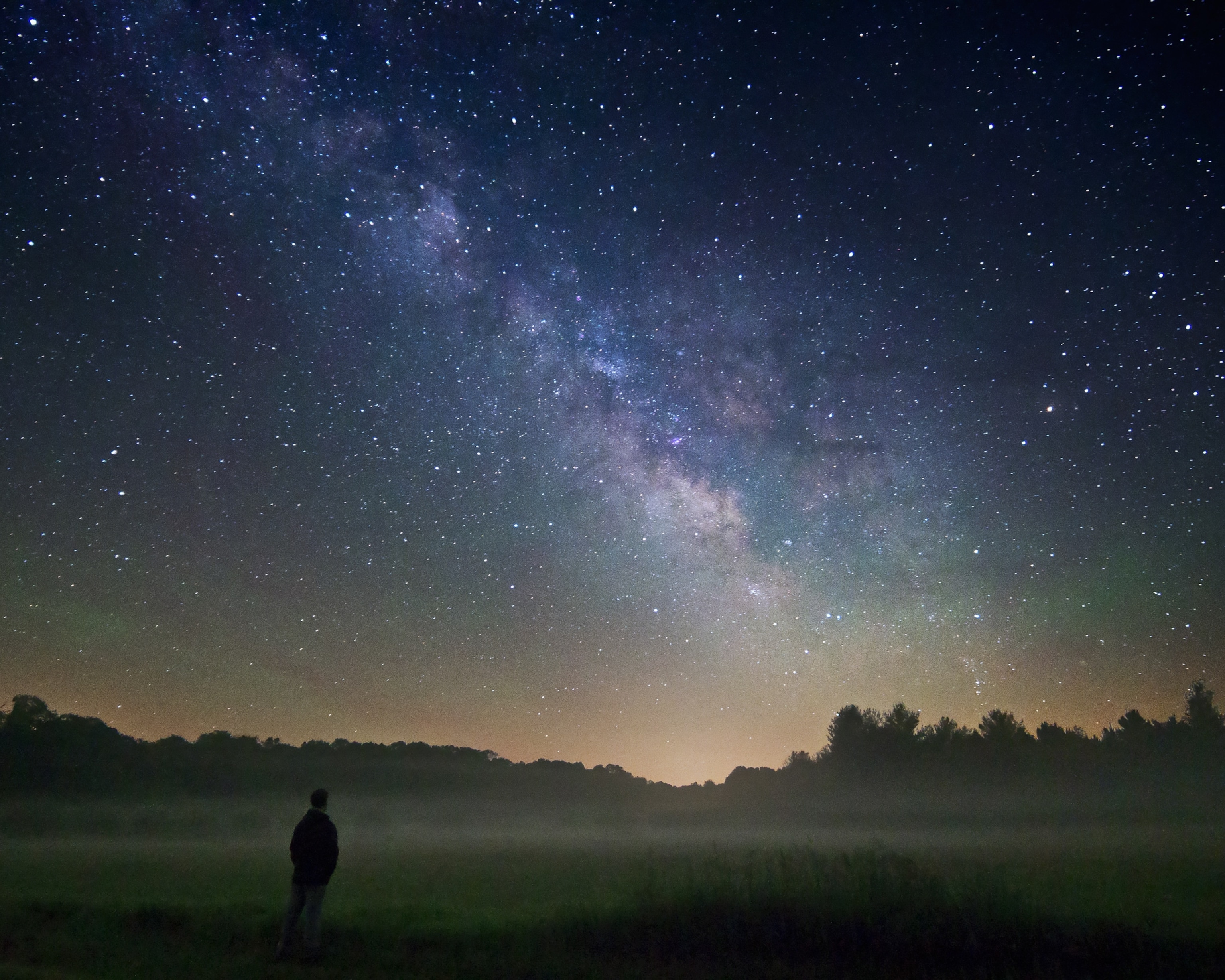 a misty fog over a field with the Milky Way in the background.