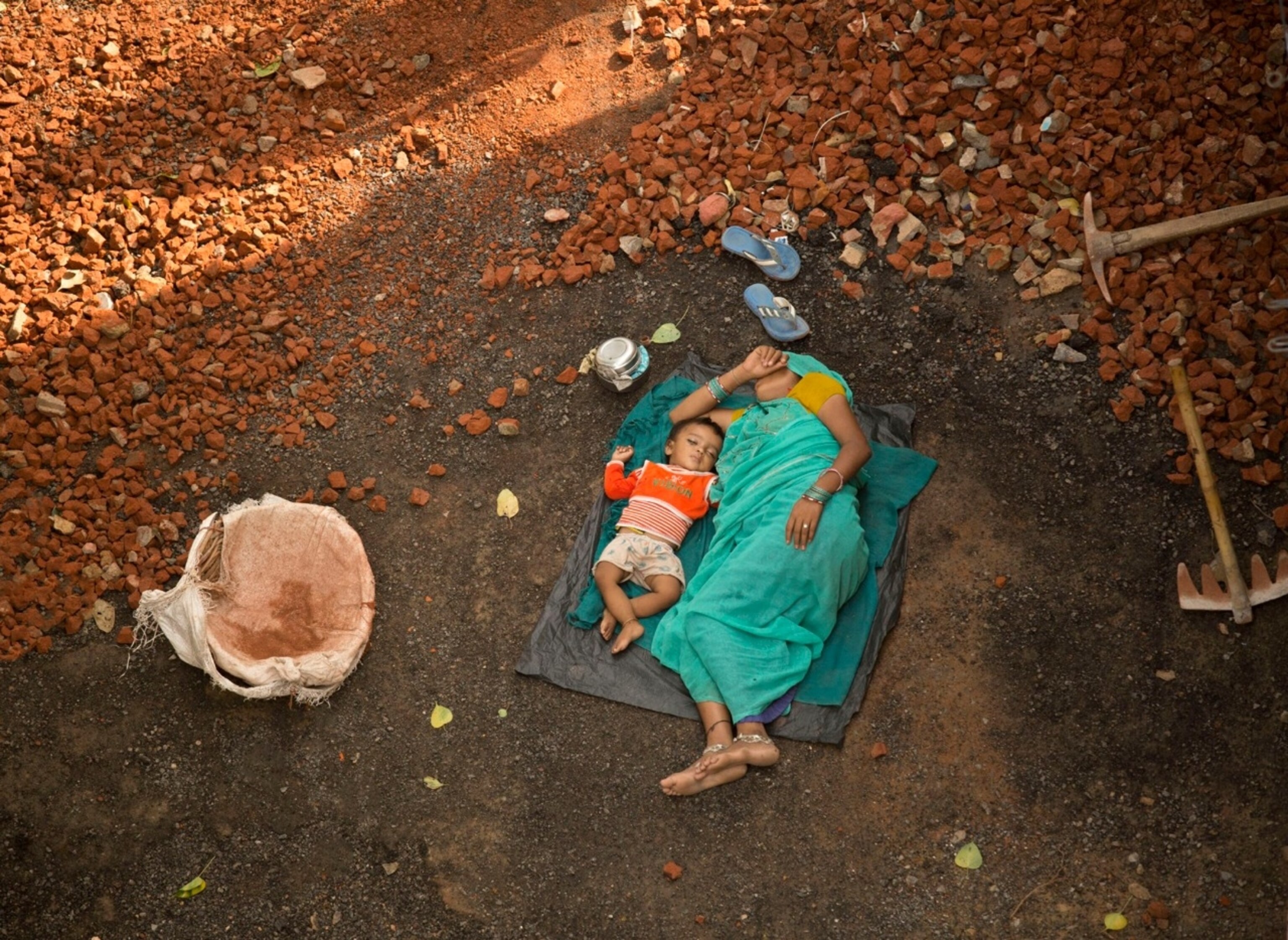 An aerial photograph of a mother taking a nap with her child on the ground in Delhi, India