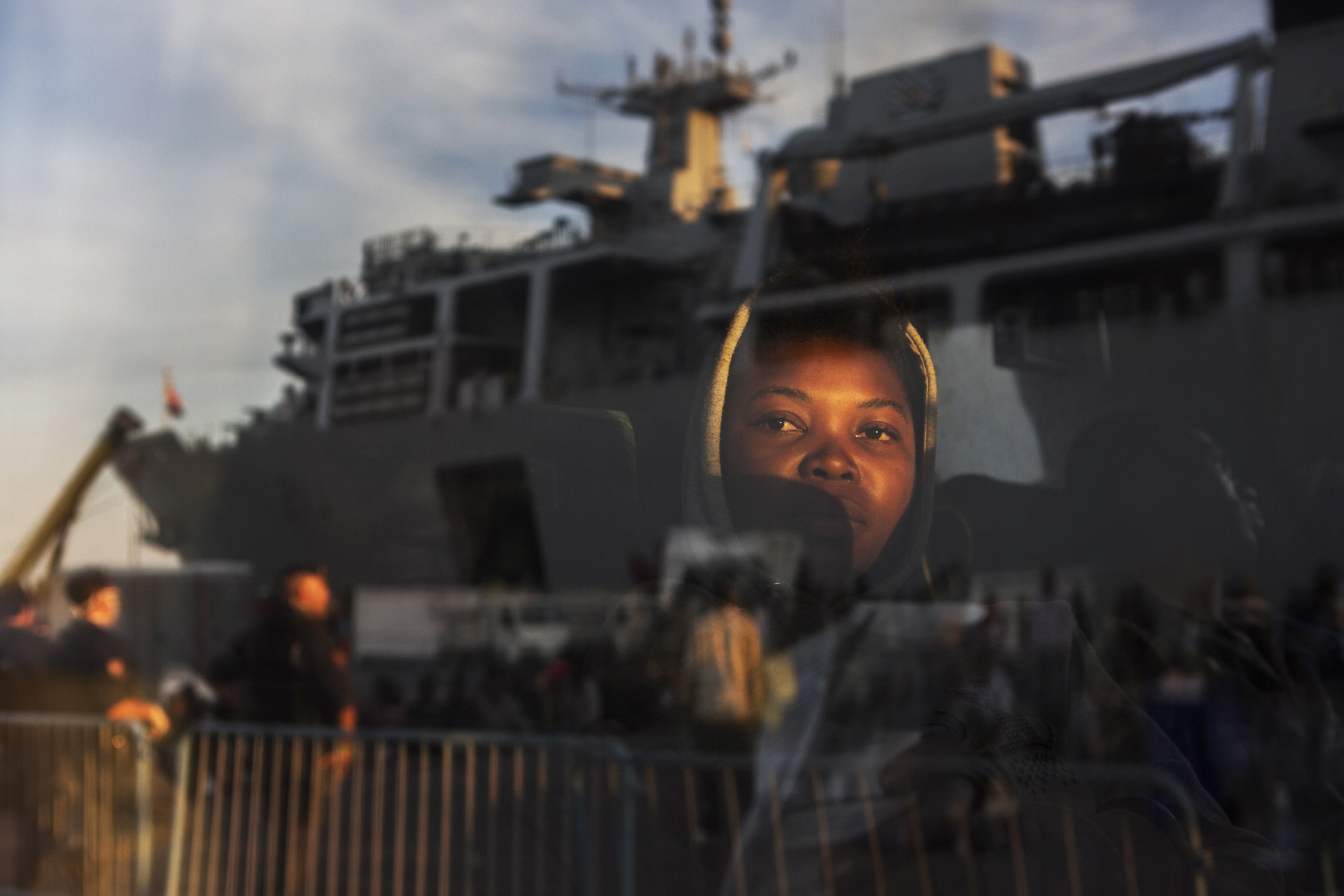migrant's face reflected in window with ship in background