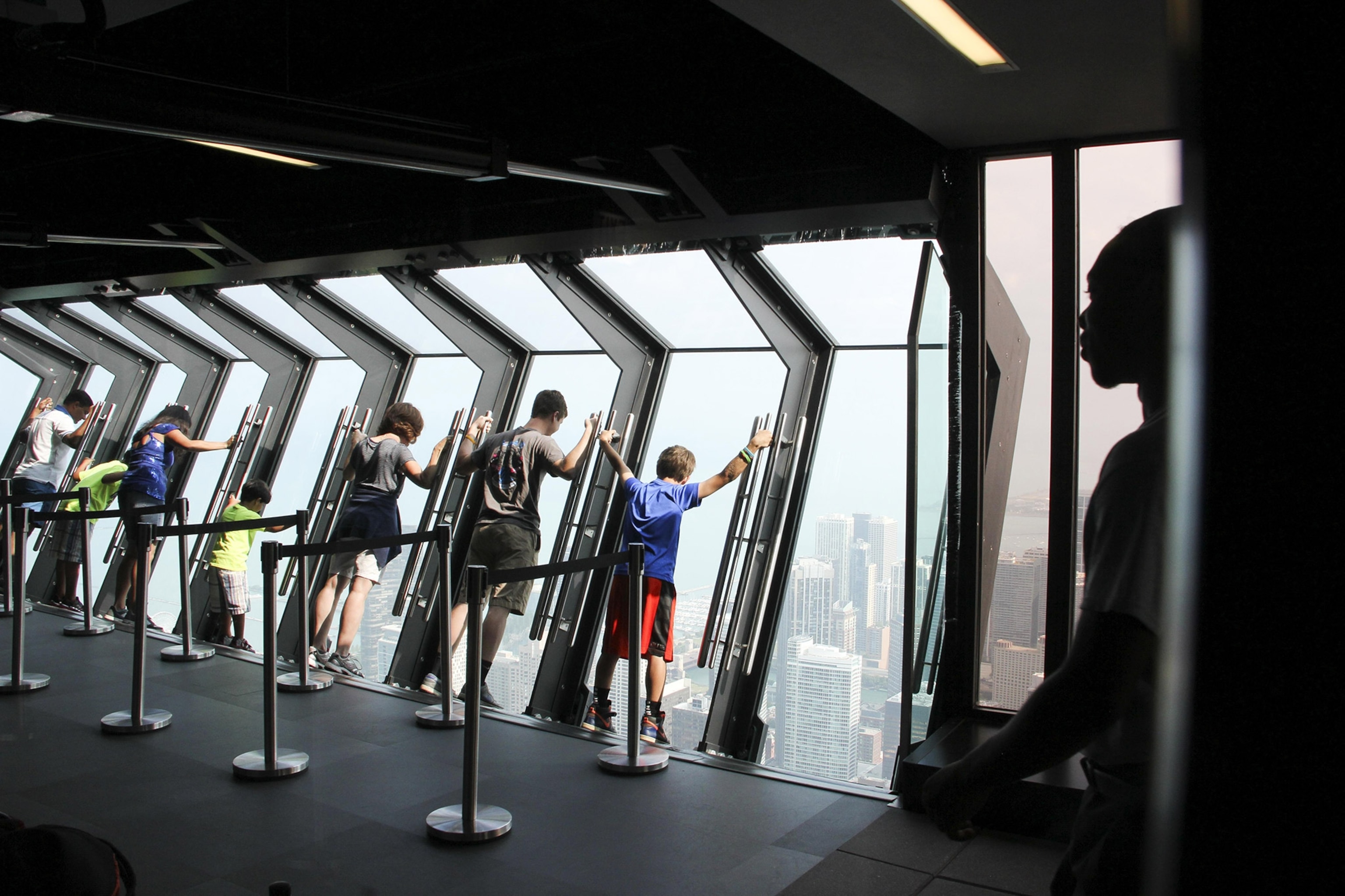 A group of people lean against tilted glass overlooking a city from a high floor