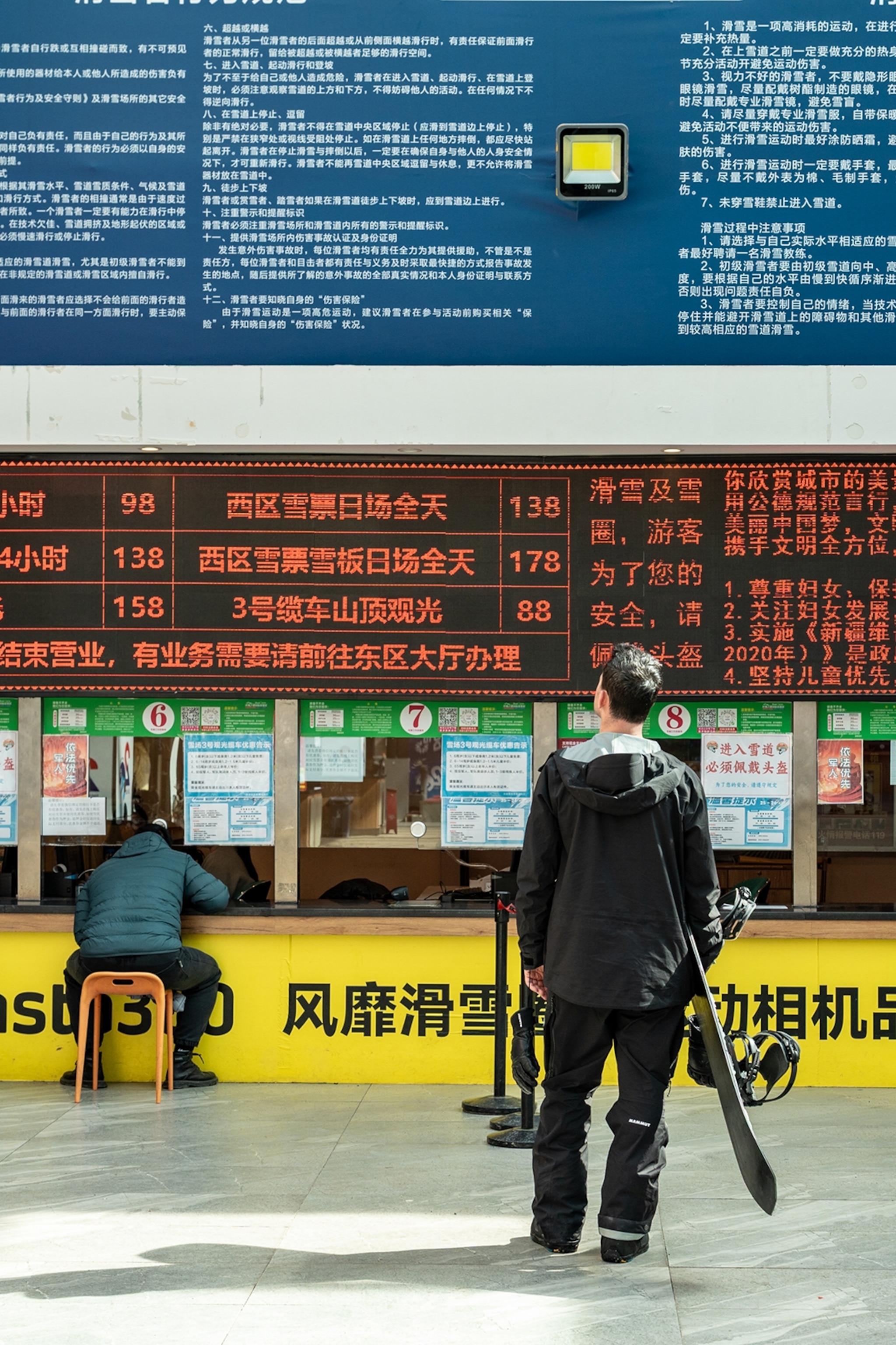 A snowboarder reading a board of announcements in a train station.