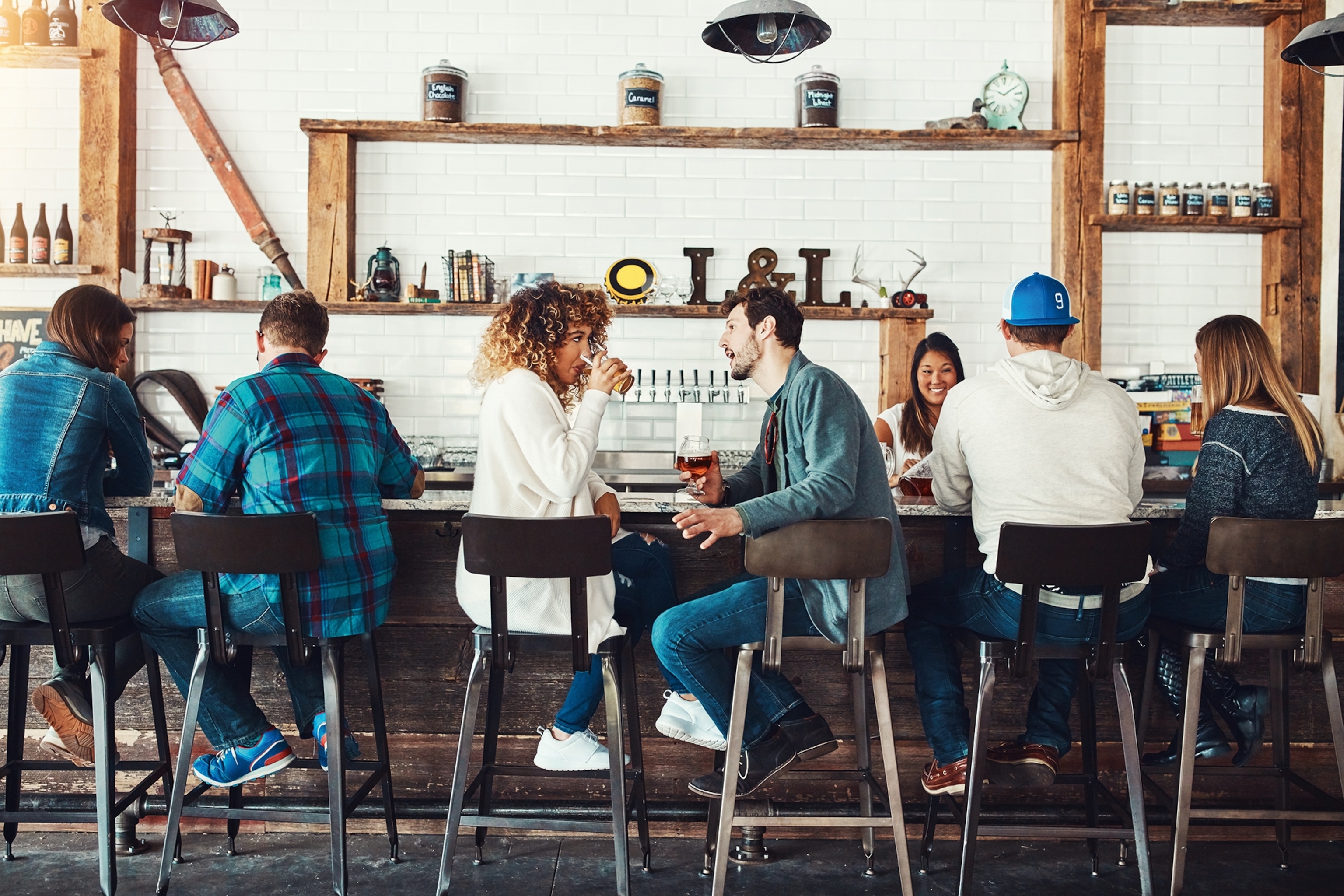 A busy and bright wooden bar counter with couples sitting on high chairs, enjoying a drink or two.