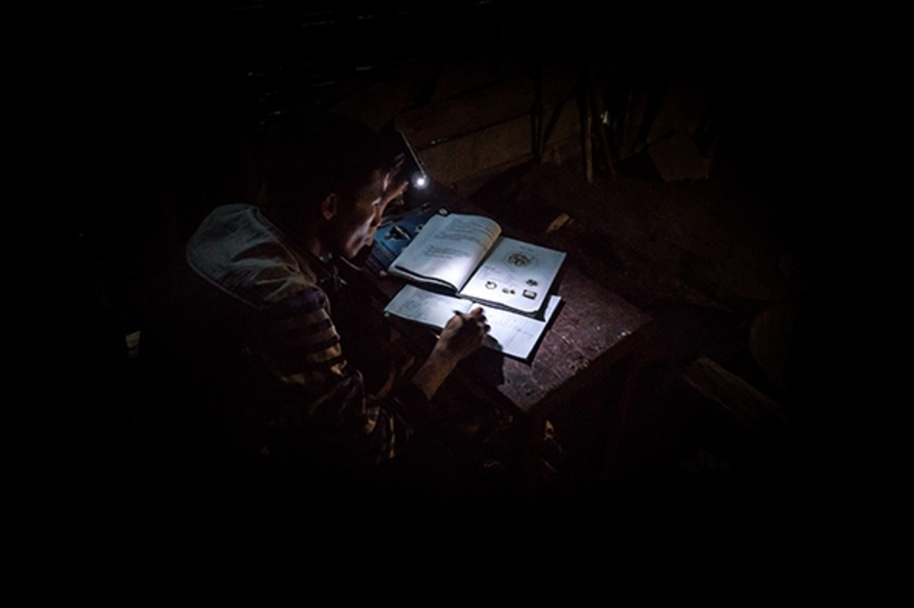 A man does his homework by the light on his cellphone in a remote Hmong village. This village has no running water or electricity, yet is located on a paved road next to power lines. Kyle Hemes biking the transect among upland communities from Kunming to Luang Prabang. Photograph by Will Stauffer-Norris