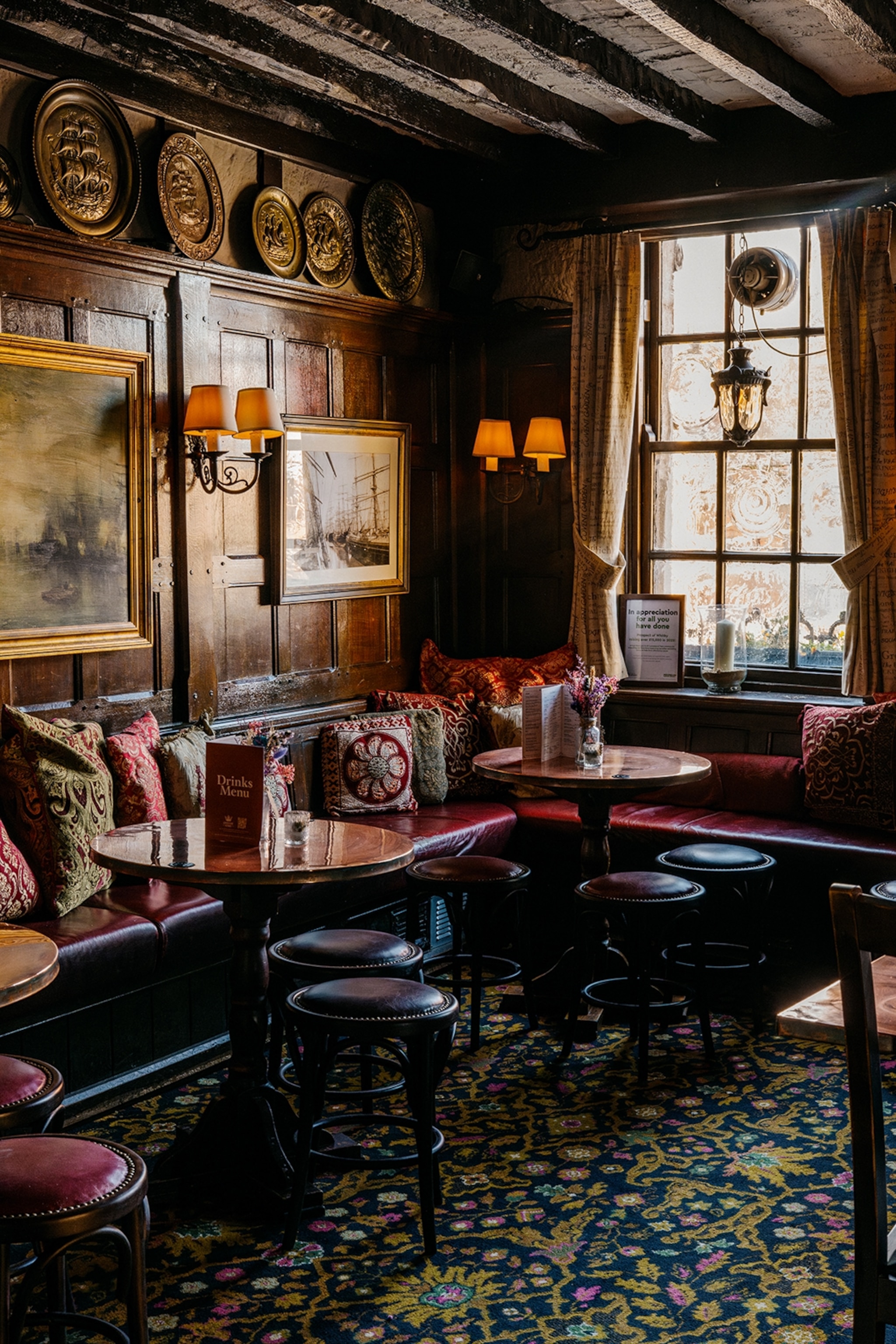 The cosy interiors of a British pub with table lamps, sofas and tall windows.