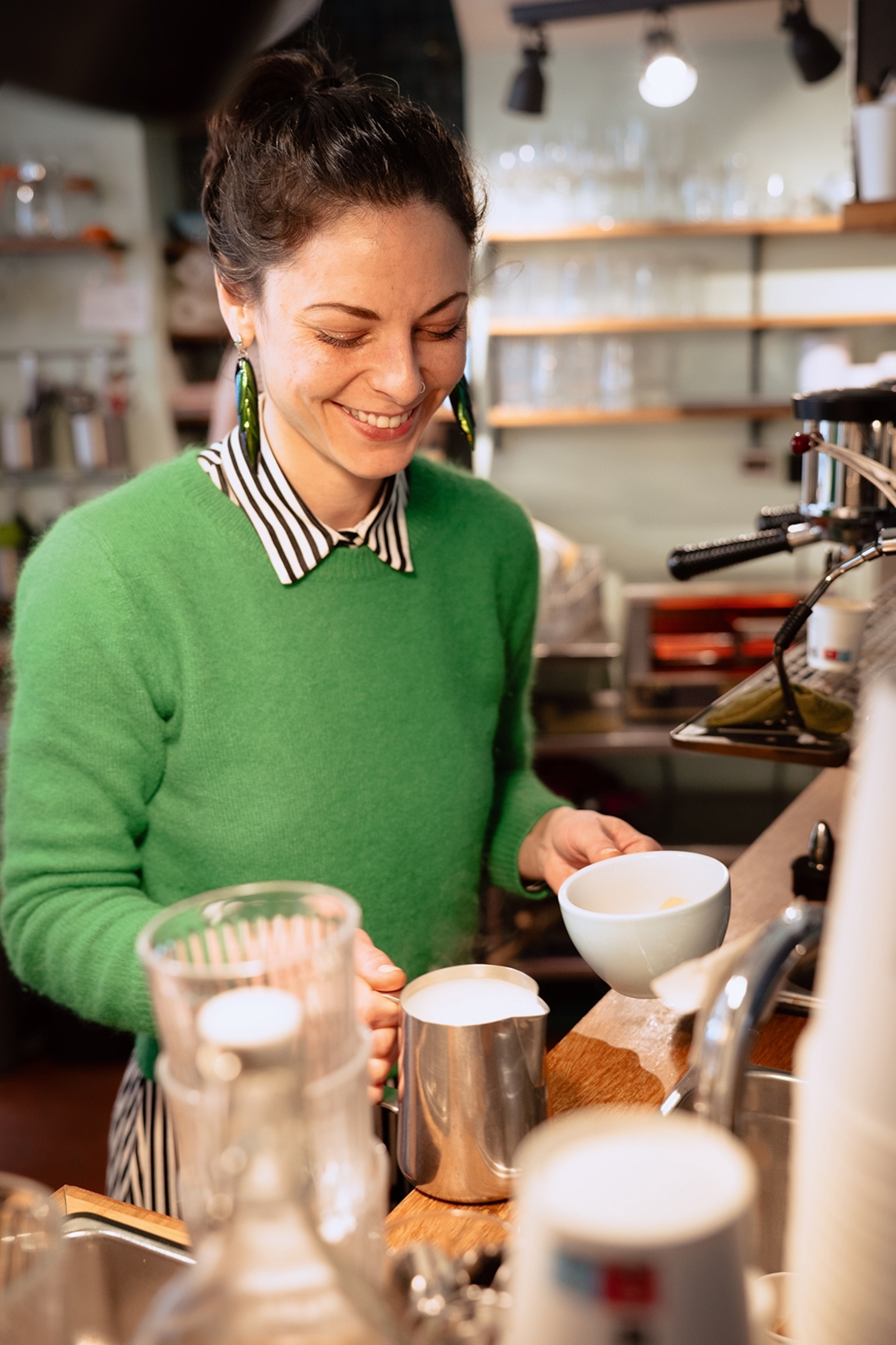 A smiling woman holds a coffee mug and a jug of milk.
