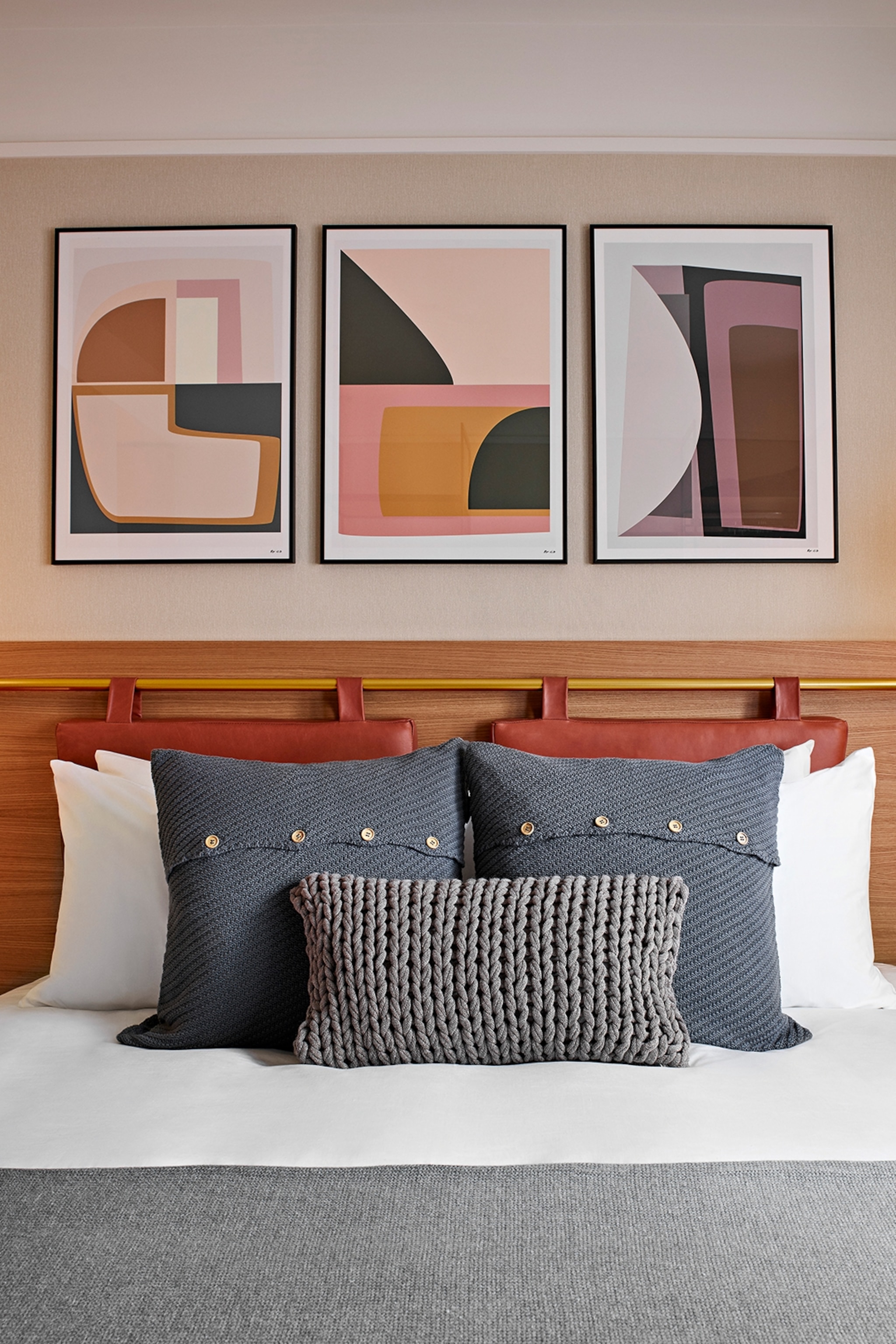A double bed with a triptych of geometric paintings hung above a golden rail.