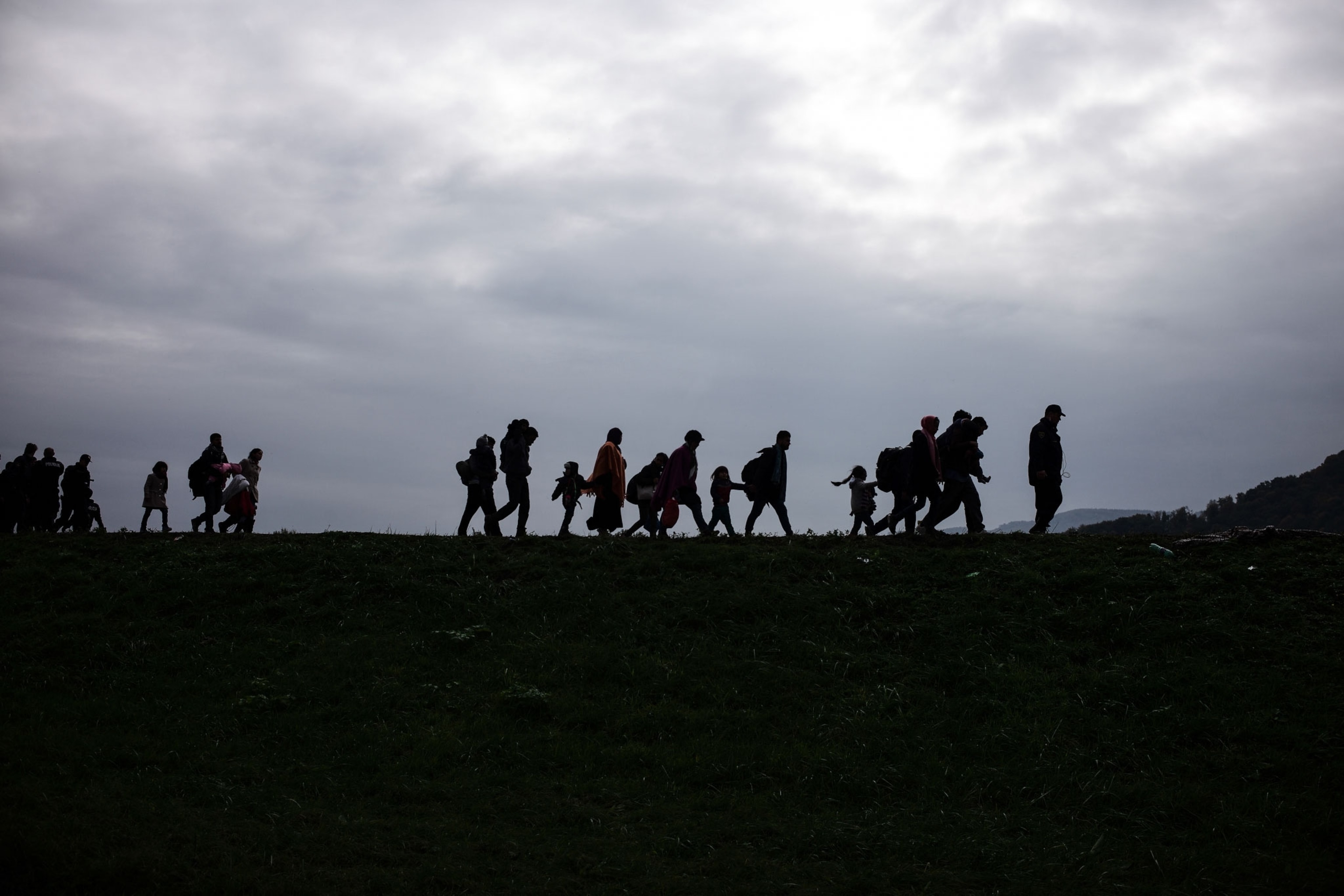 refugees silhouetted against the sky as they walk