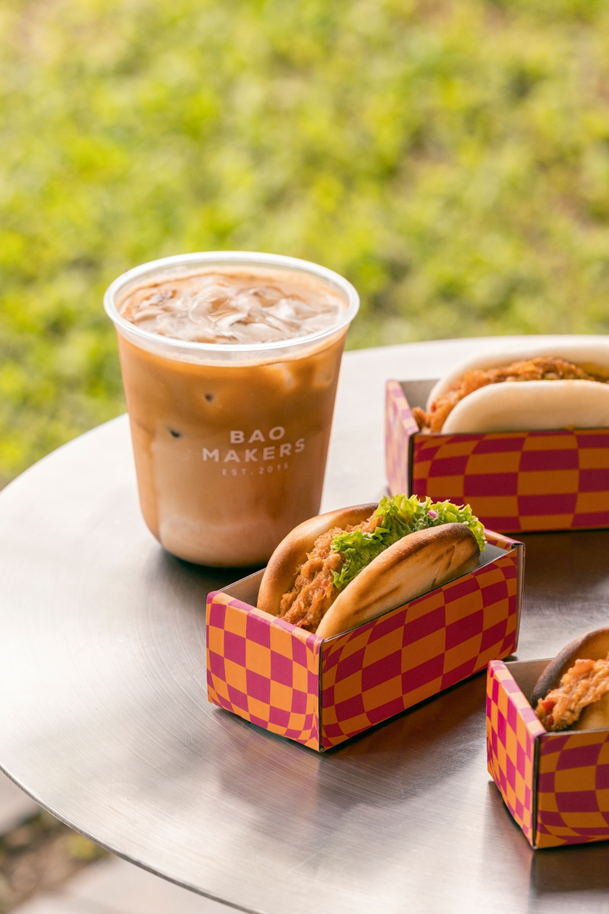A close-up of bao buns filled with chilli crab in individual carton pockets on a metallic outdoor table.