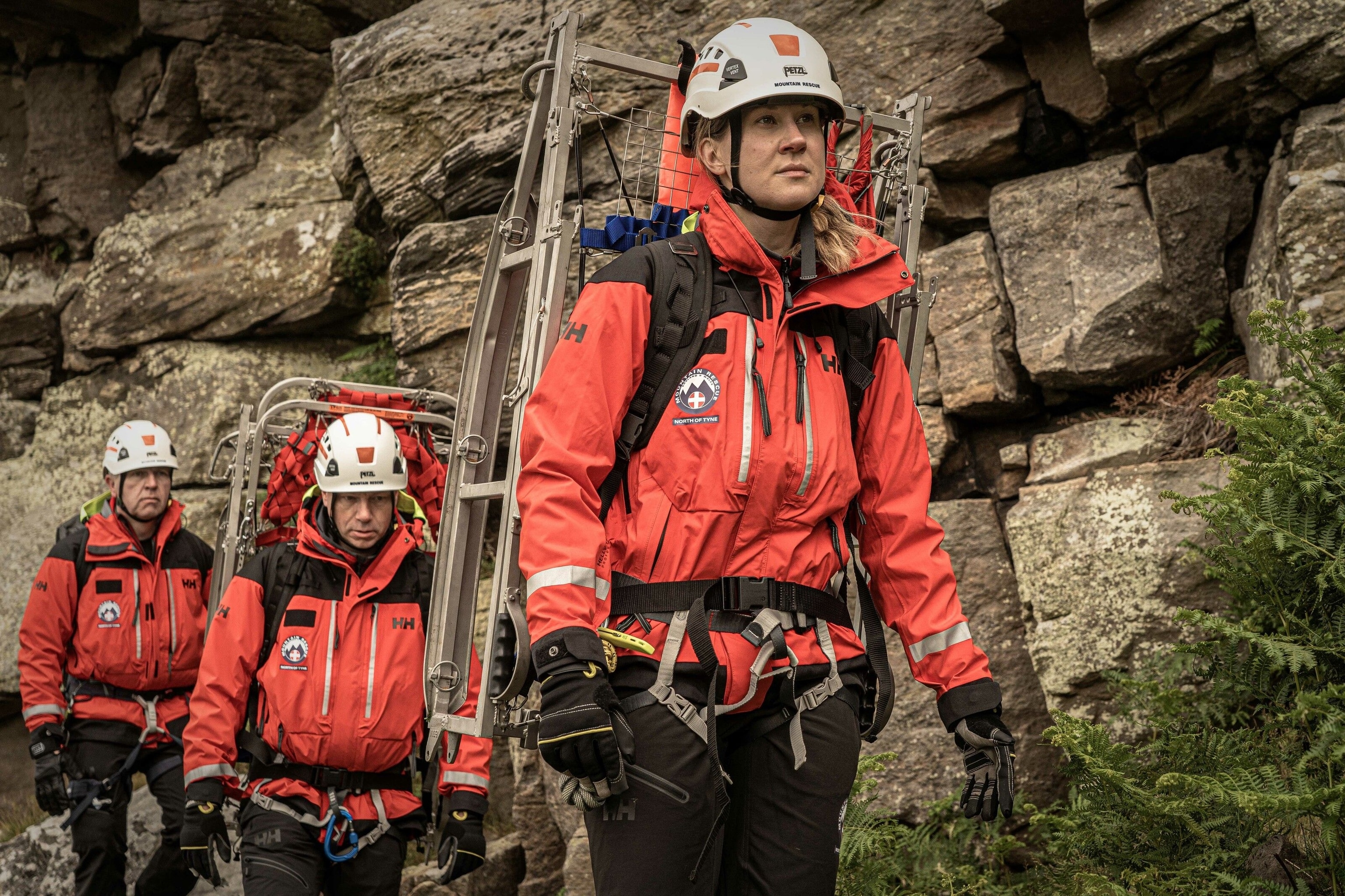 People walking in red Helly Hansen coats, carrying mountain rescue kit.