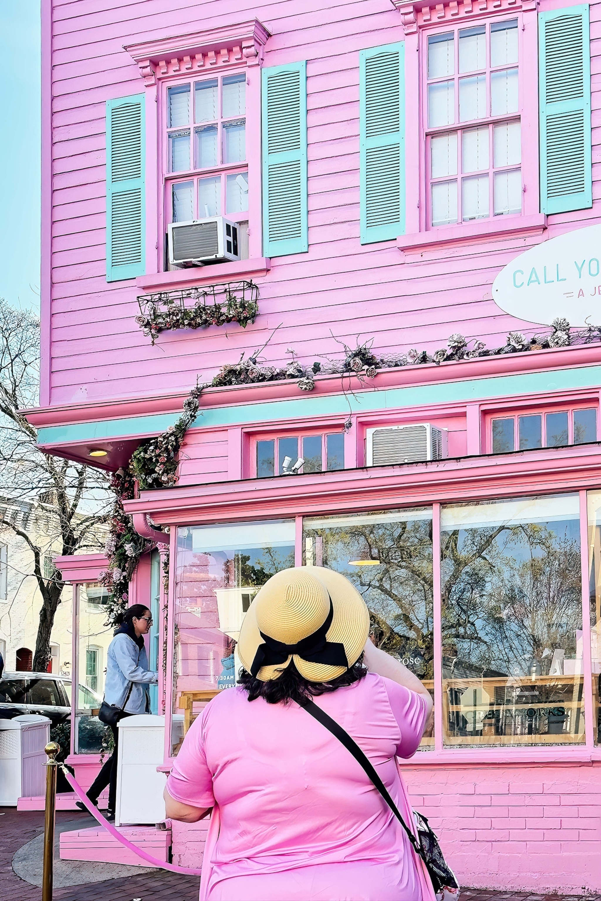 A woman with a straw hat stands infront of a pink store.