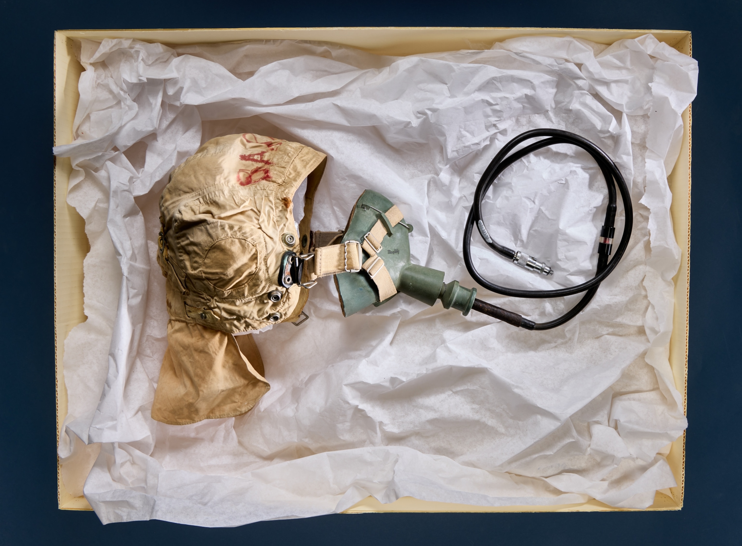 Mask with rubber tubing on paper tissue in the archival carton box.