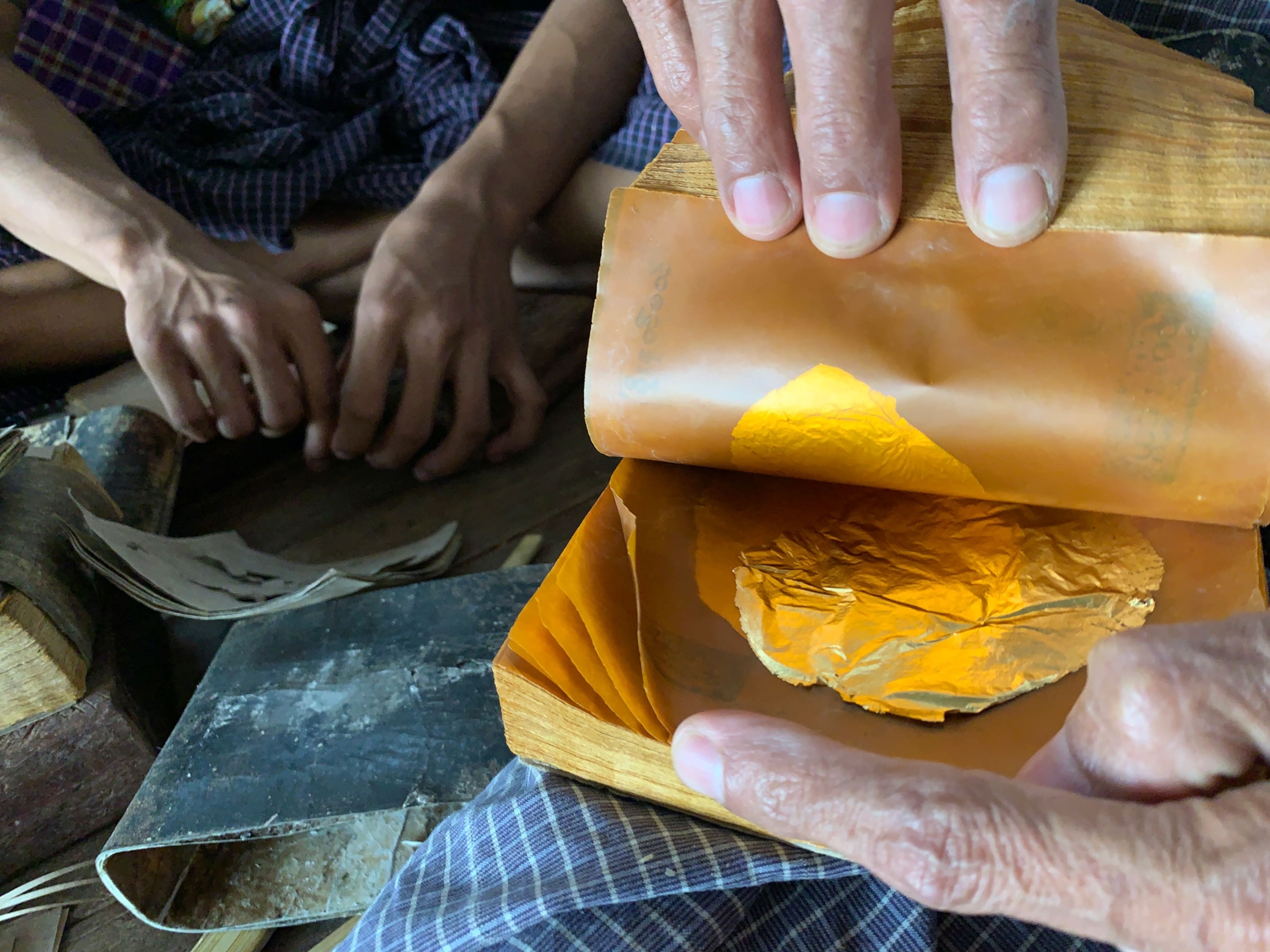 Thin pieces of gold are between sheets of waxy looking paper