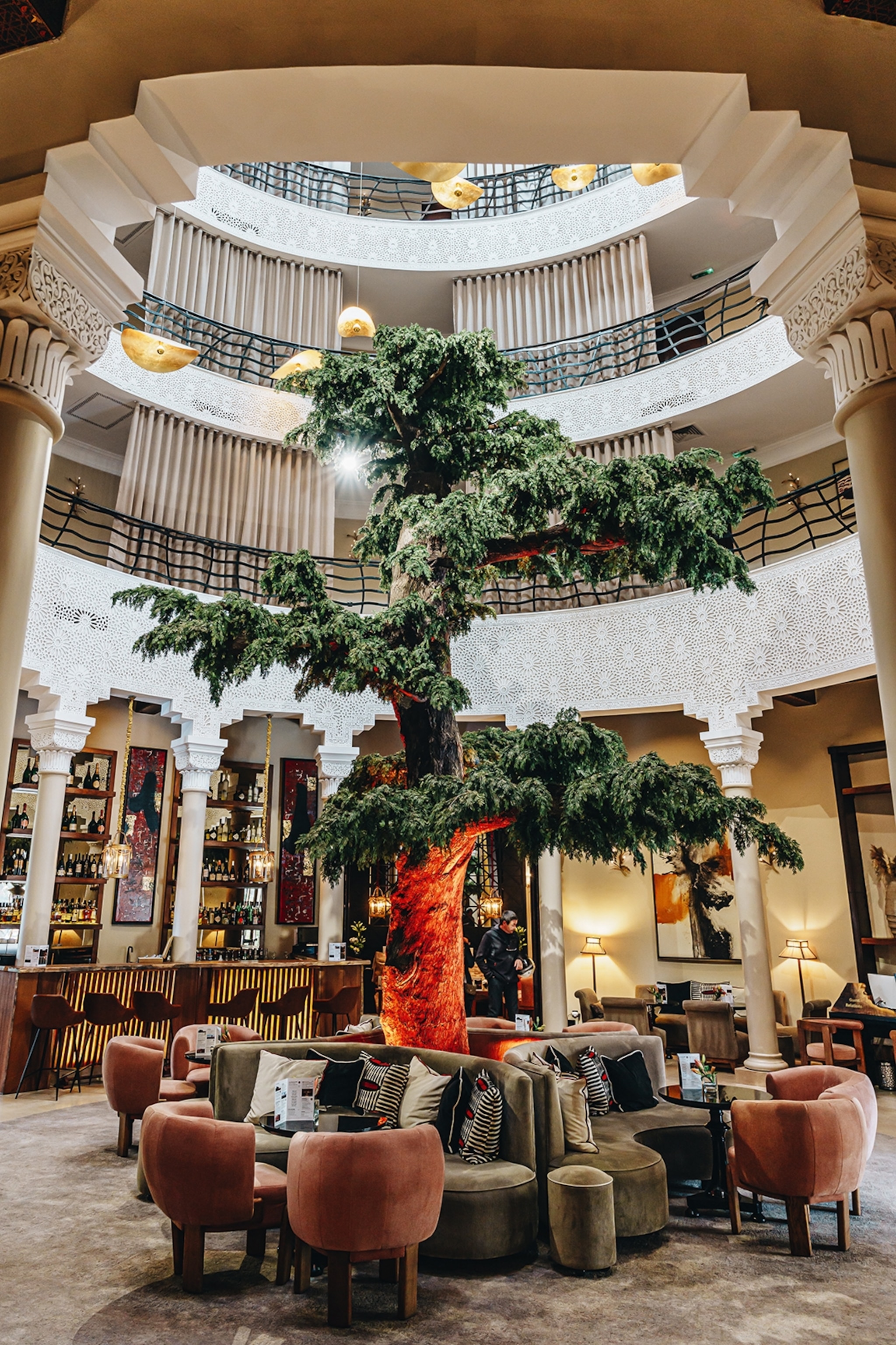 The interior of an atrium-like bar with a tall bonsai tree int the centre.